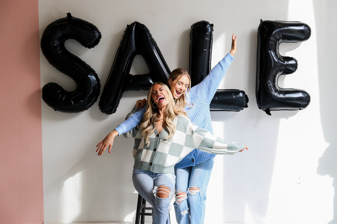 two models in cute sweaters and jeans in front of a sale sign