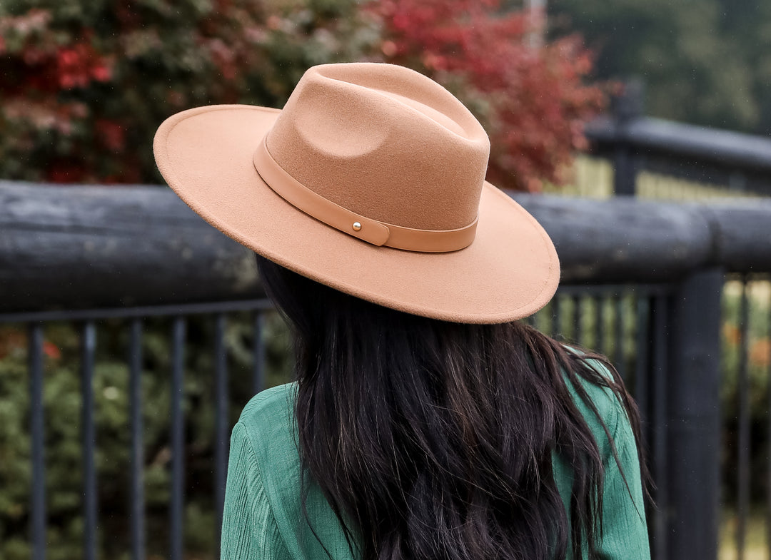 model with dark hair wearing a tan felt wide brim hat with a scenic background