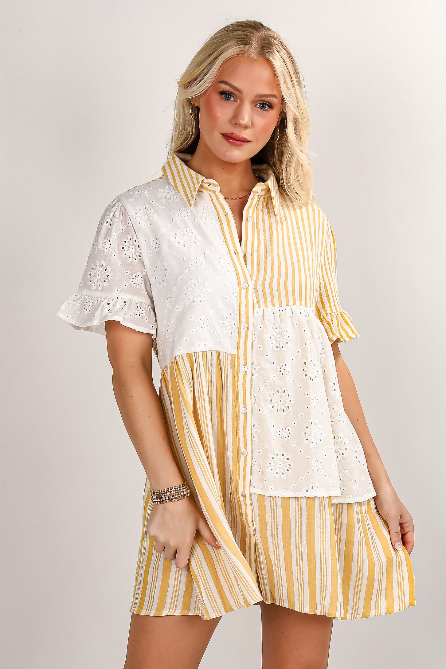 Woman wearing a yellow and white striped dress with lace details on a plain background