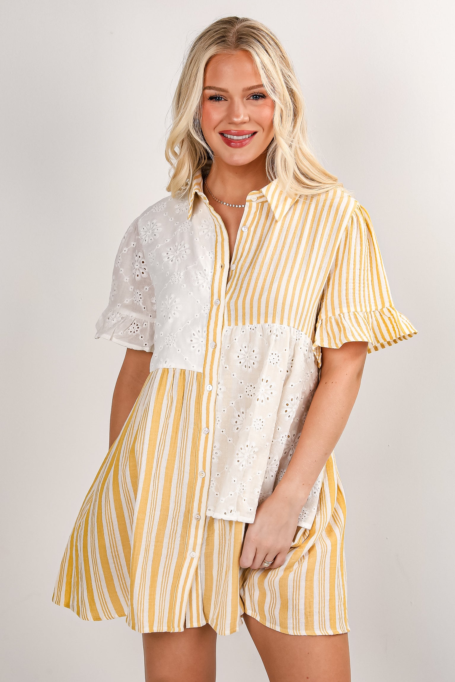 Woman wearing a yellow and white striped dress with lace details on a plain background