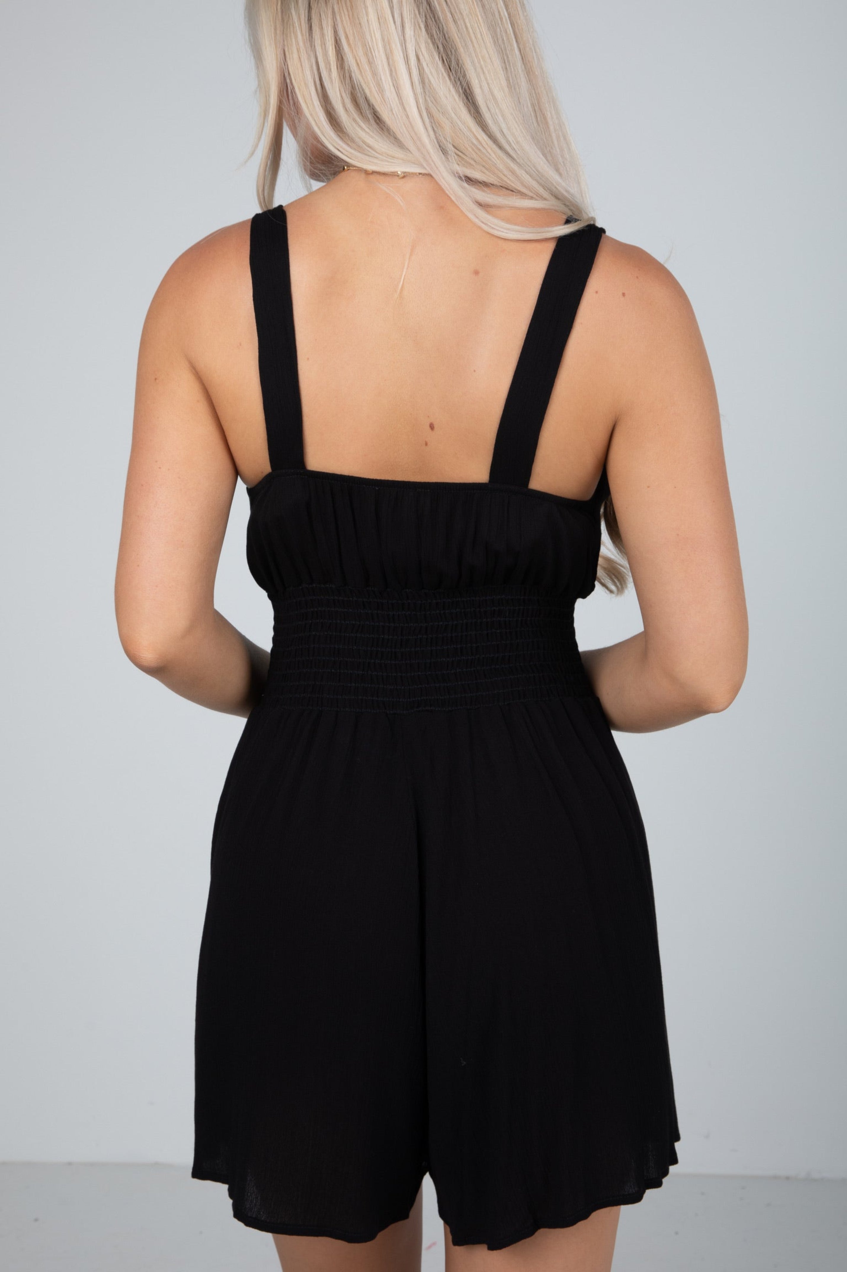 Person wearing a black romper against a gray background