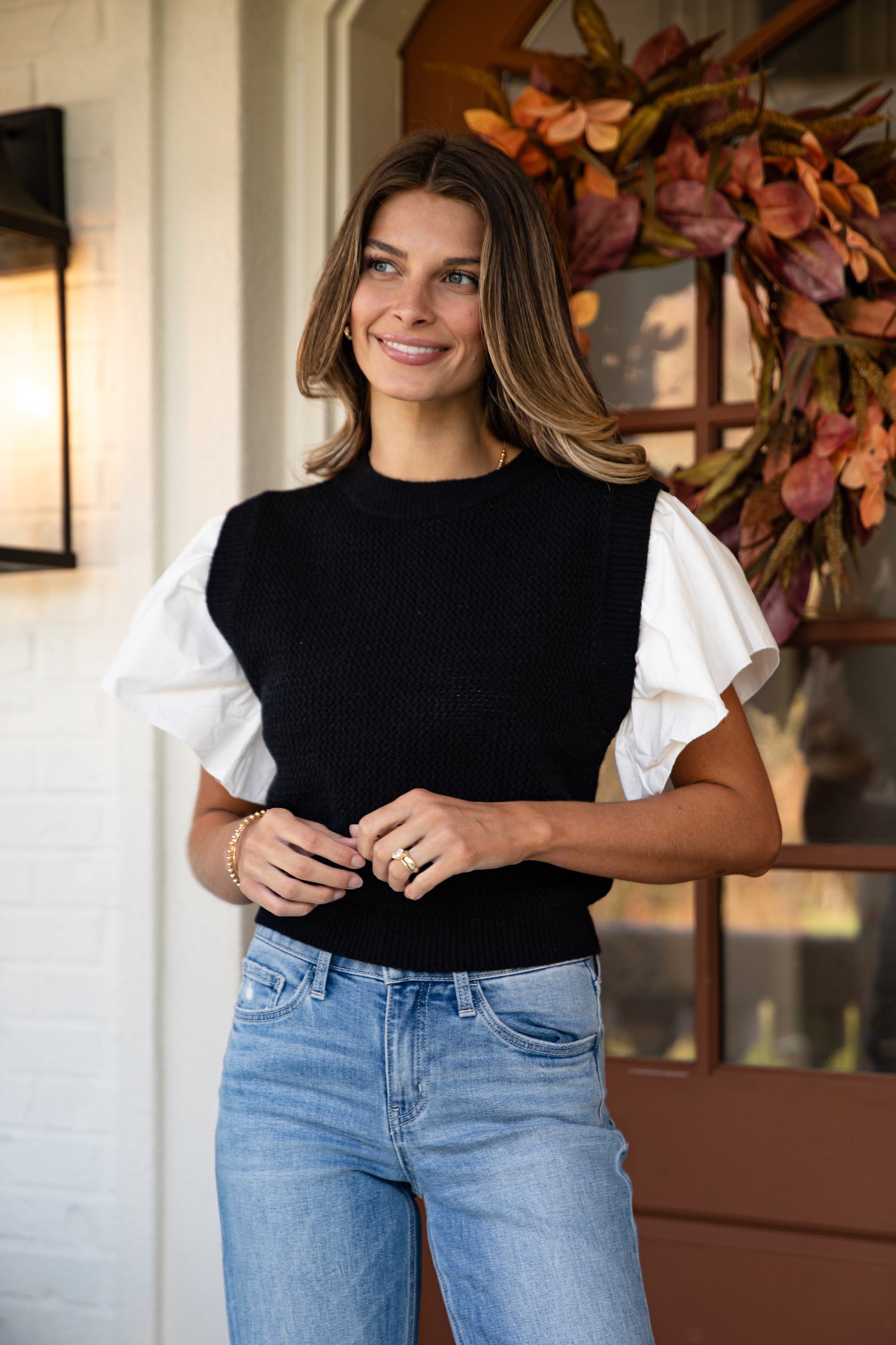 Woman wearing a black and white top with blue jeans standing indoors.