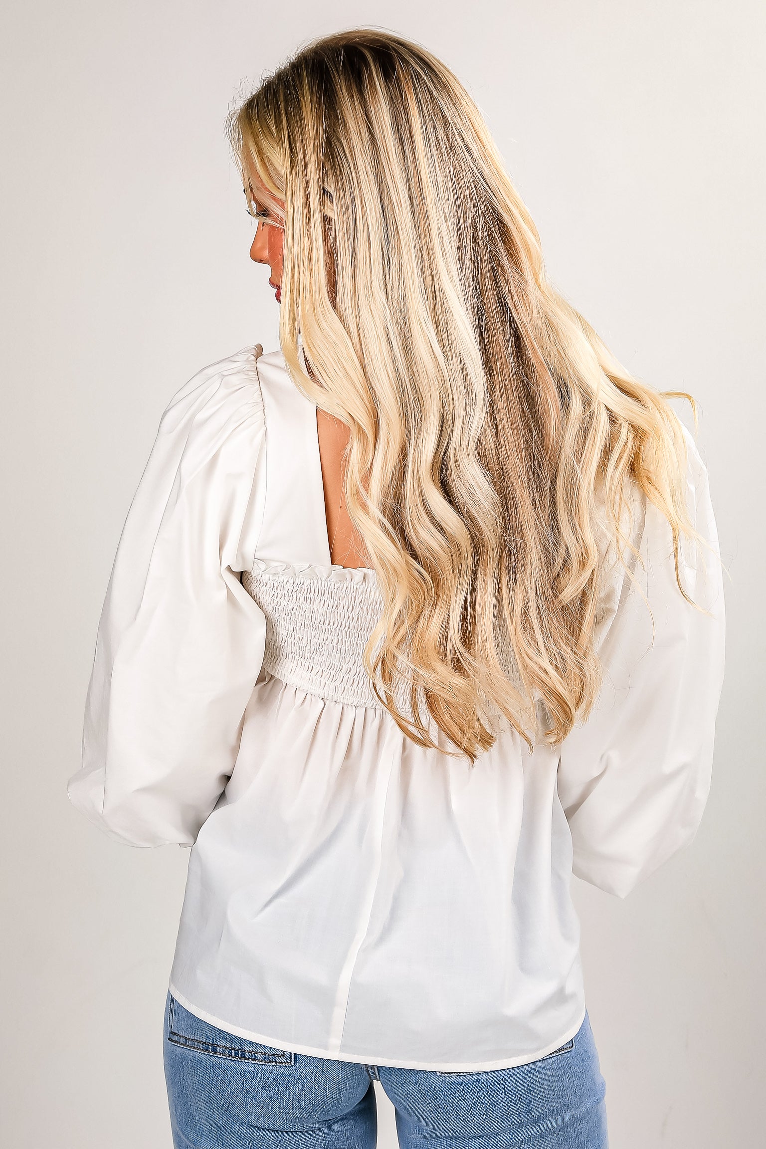 Woman wearing a white blouse and blue jeans against a plain background