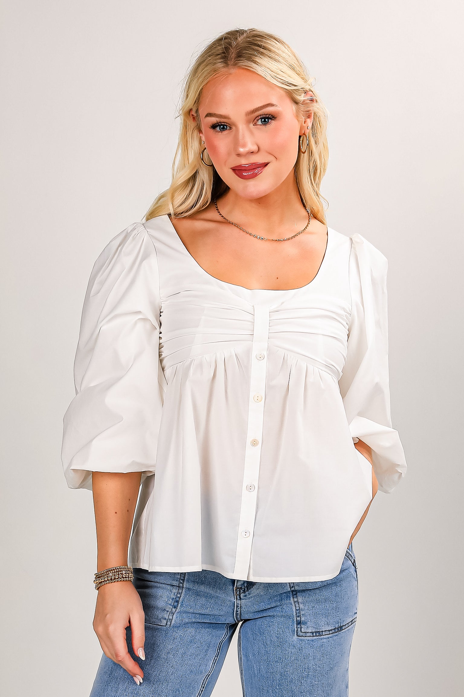 Woman wearing a white blouse and blue jeans against a plain background