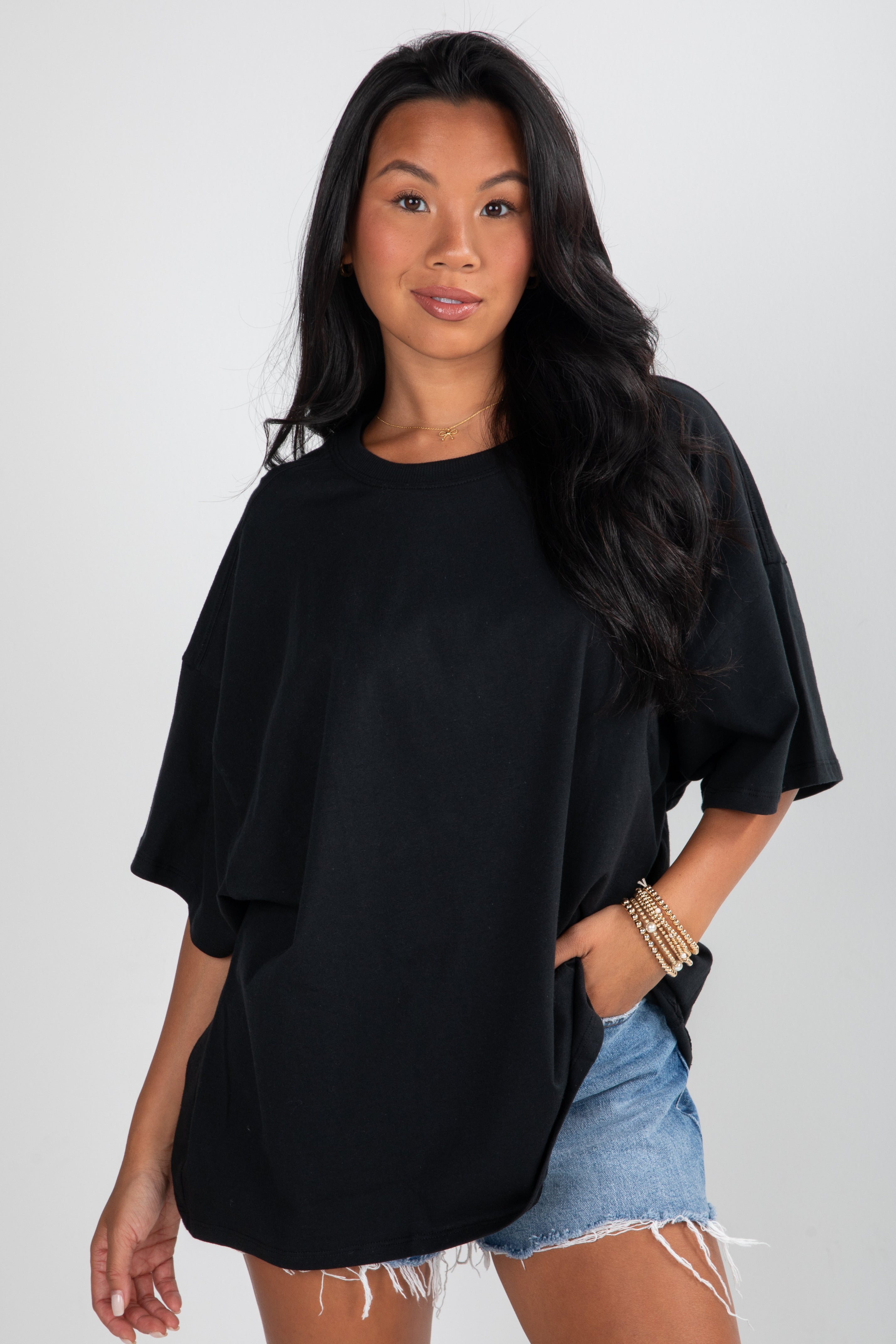 Woman wearing a black oversized shirt and denim shorts on a plain background
