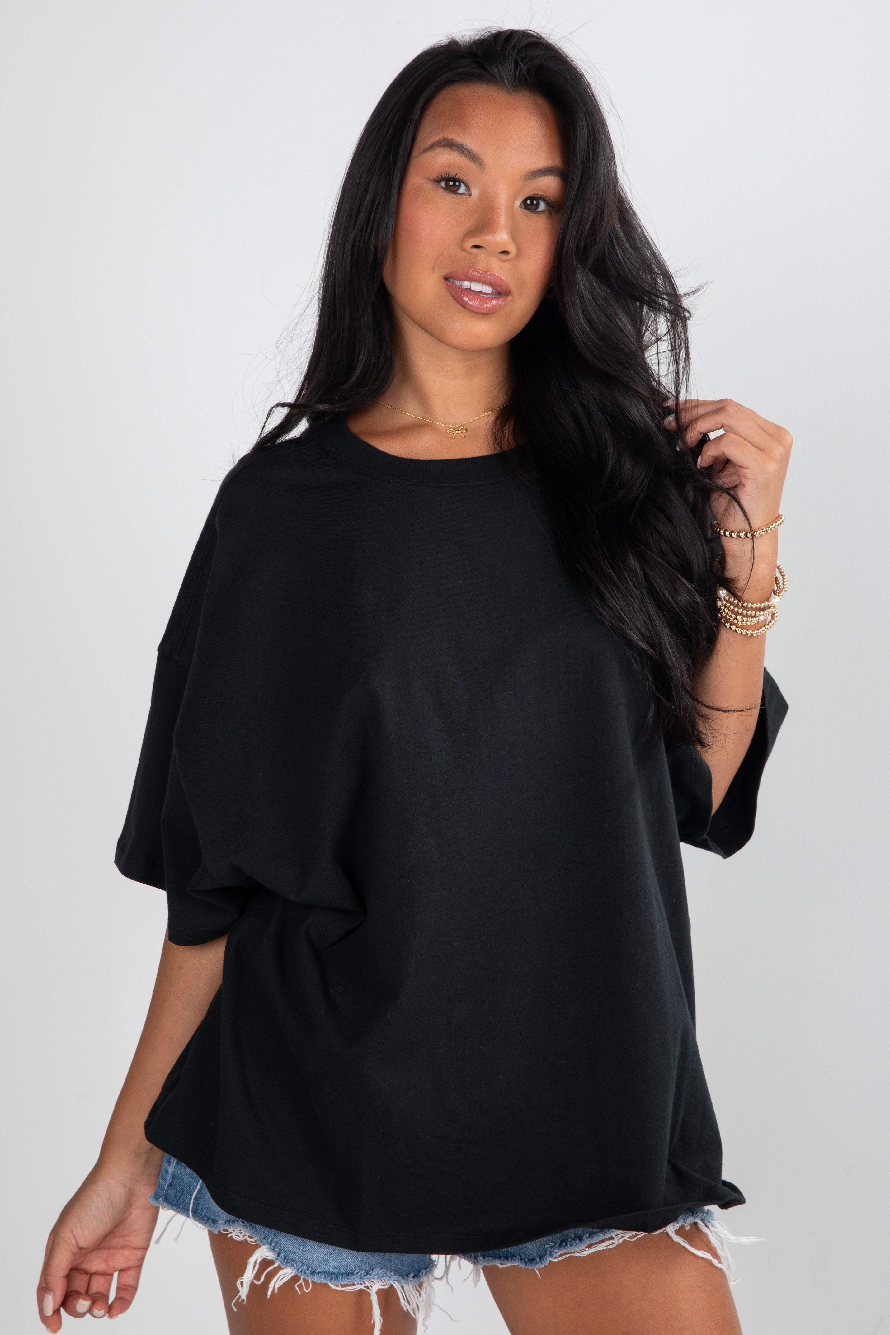 Woman wearing a black oversized top and denim shorts on a white background
