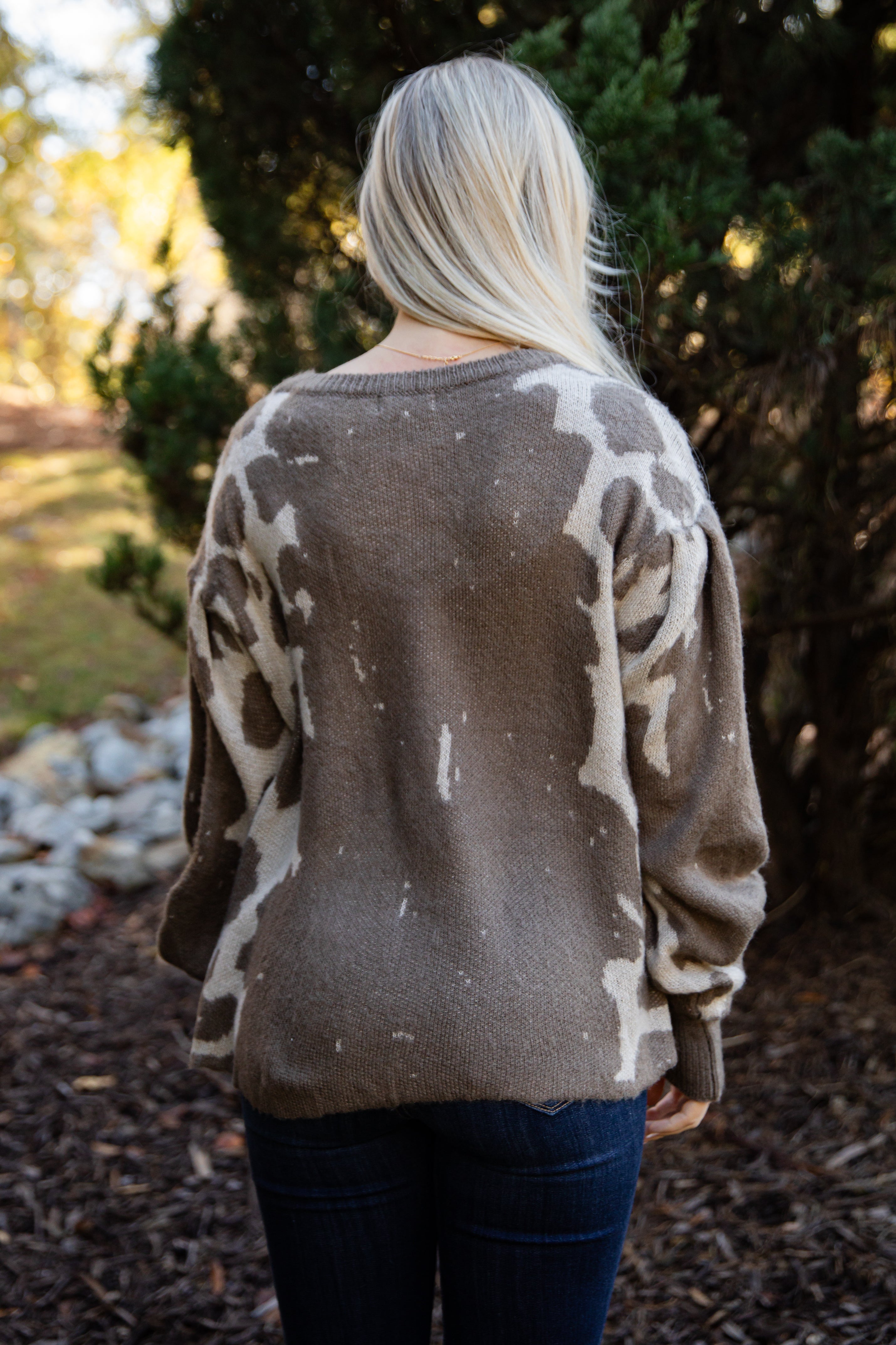 Person wearing a brown sweater with white abstract patterns outdoors.