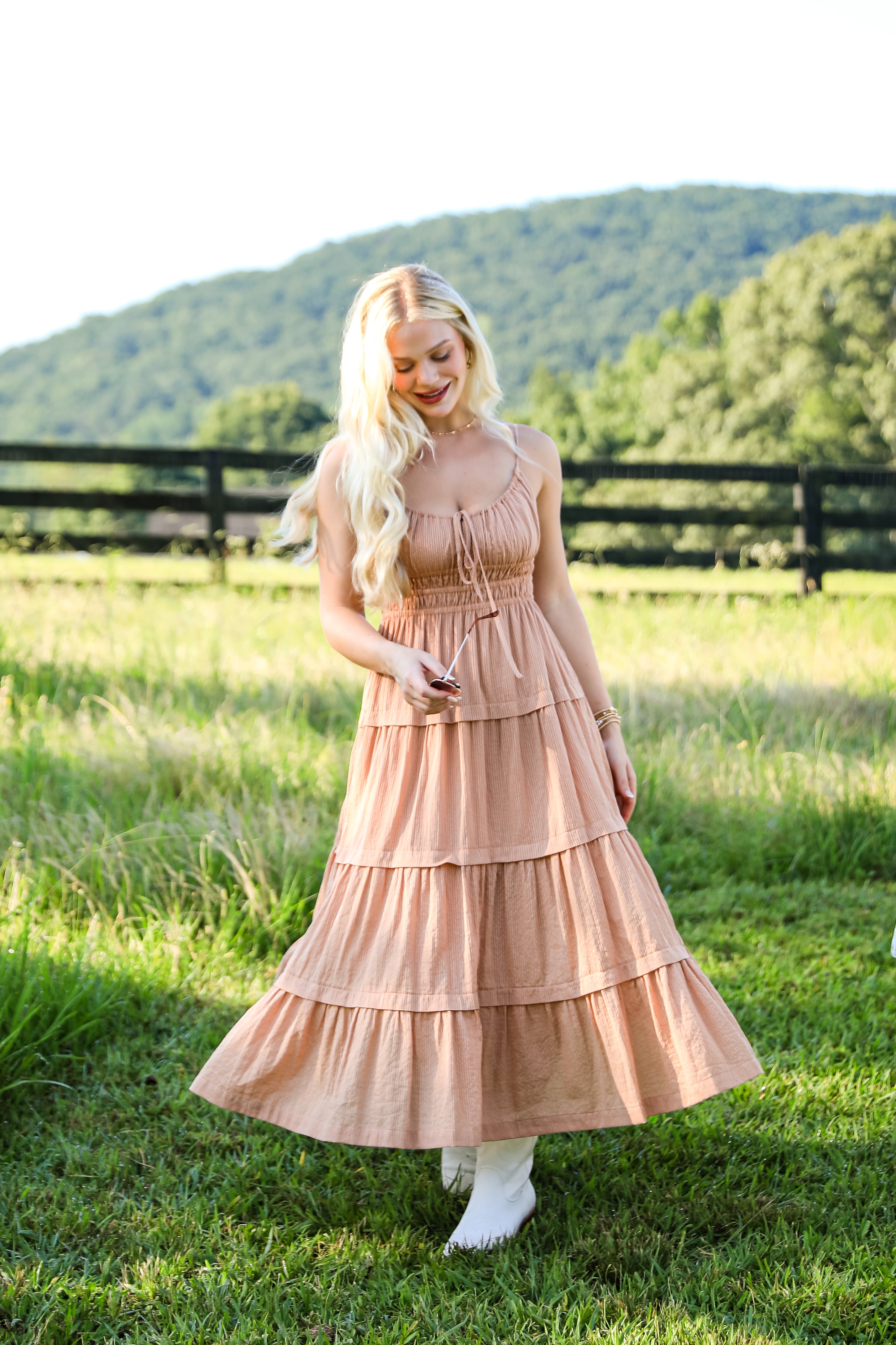Woman in a peach dress standing in a grassy field with mountains in the background