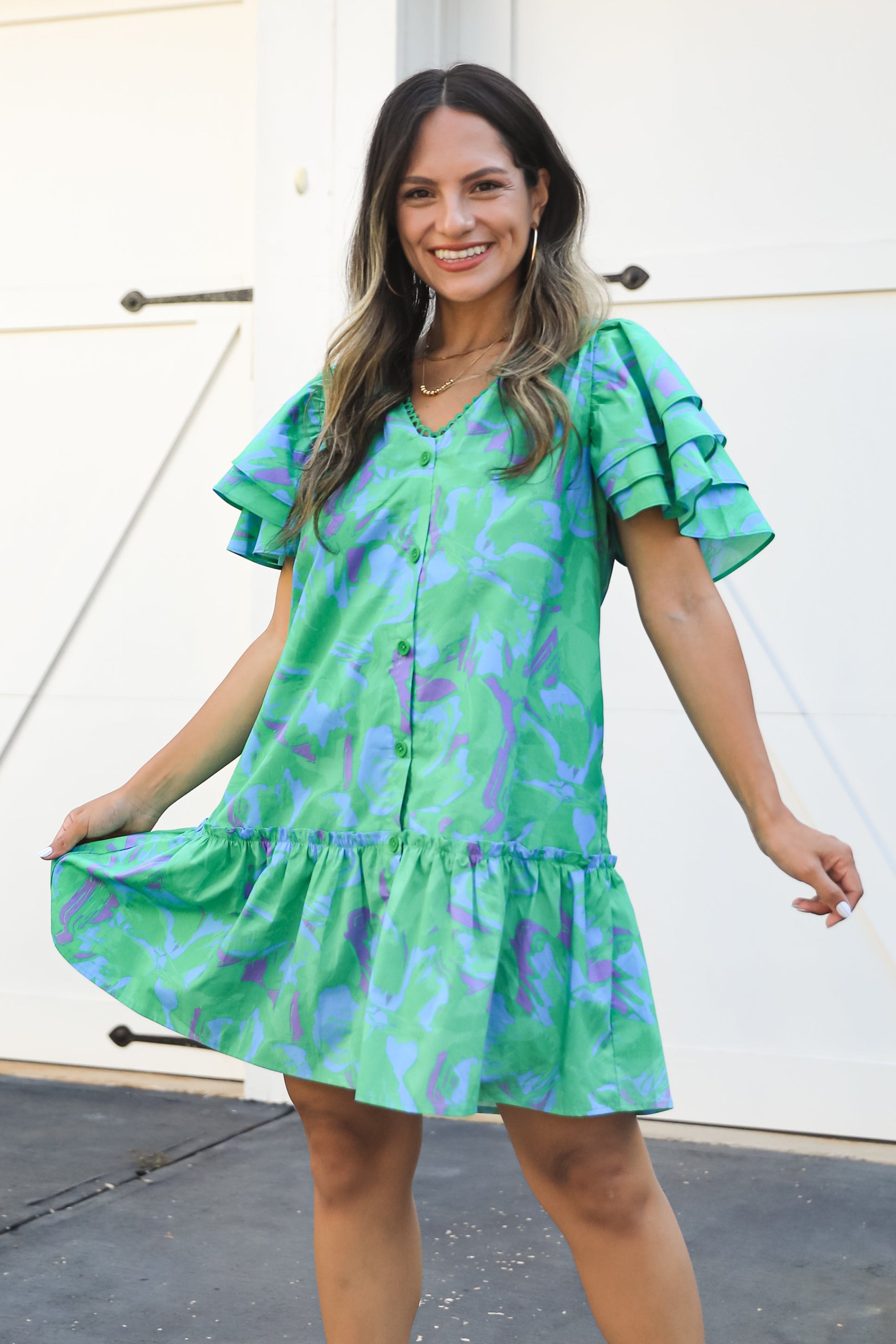 Woman wearing a green floral dress and white boots standing in front of white doors.