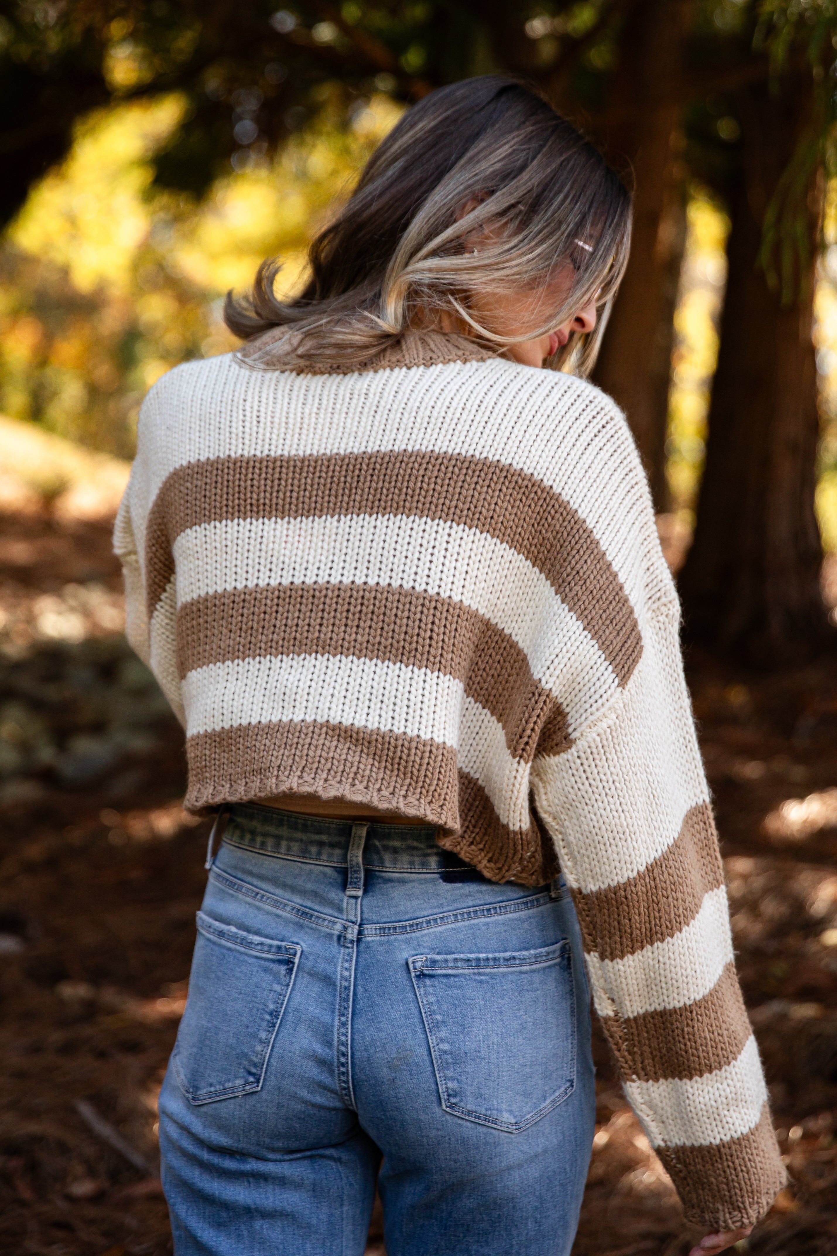 Person wearing a striped sweater and blue jeans standing in a forest