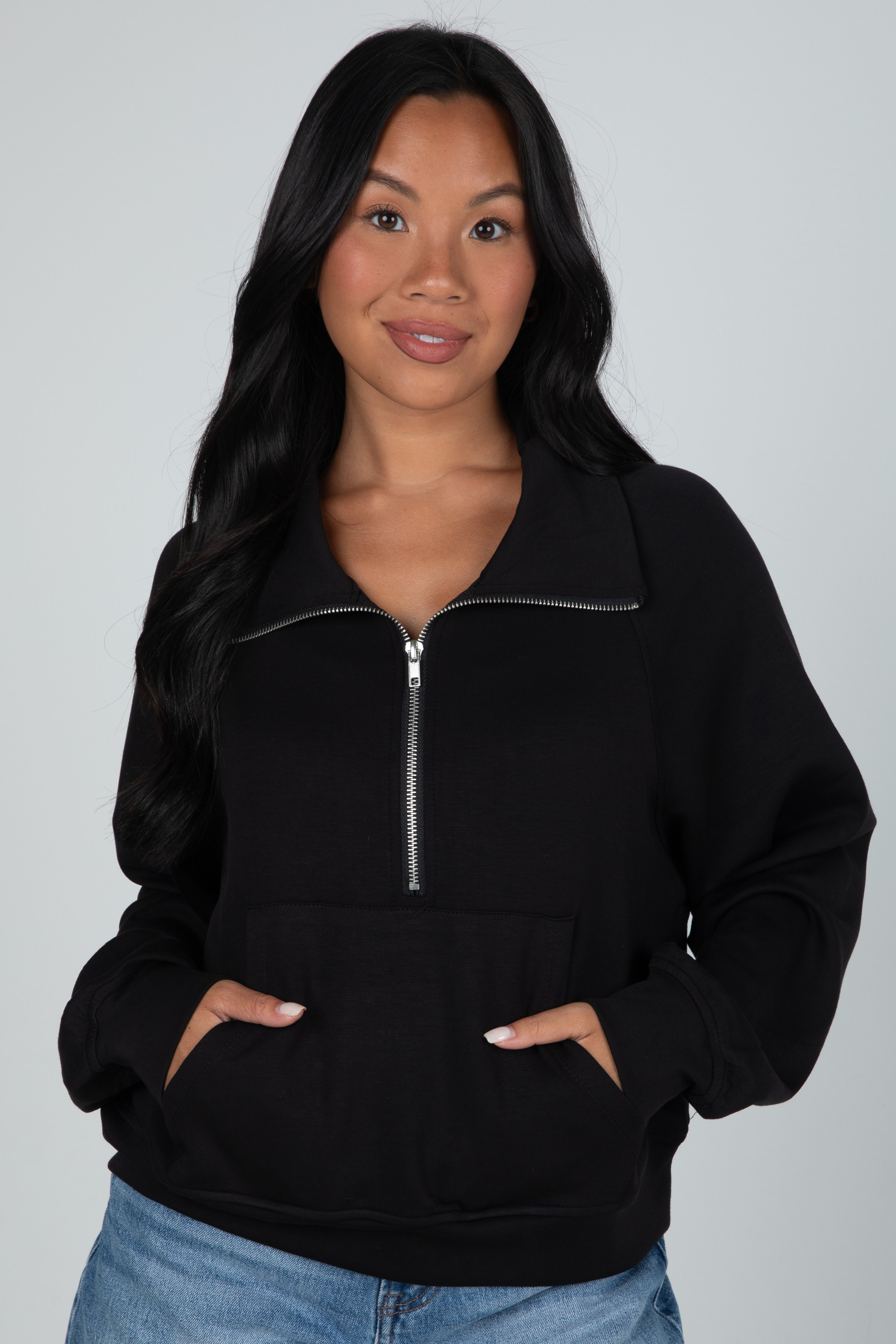 Woman wearing a black zip-up hoodie against a gray background