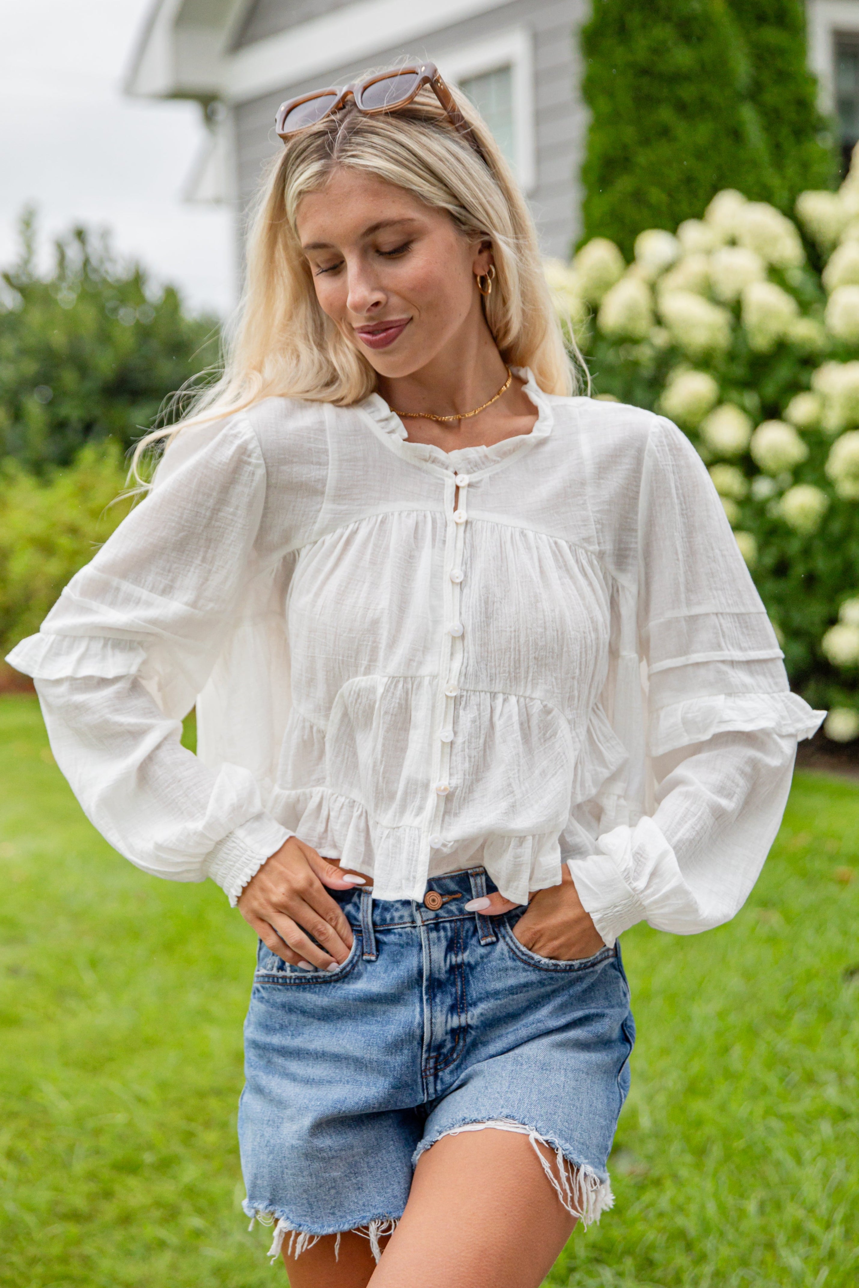 Woman wearing a white blouse and denim shorts standing outdoors.
