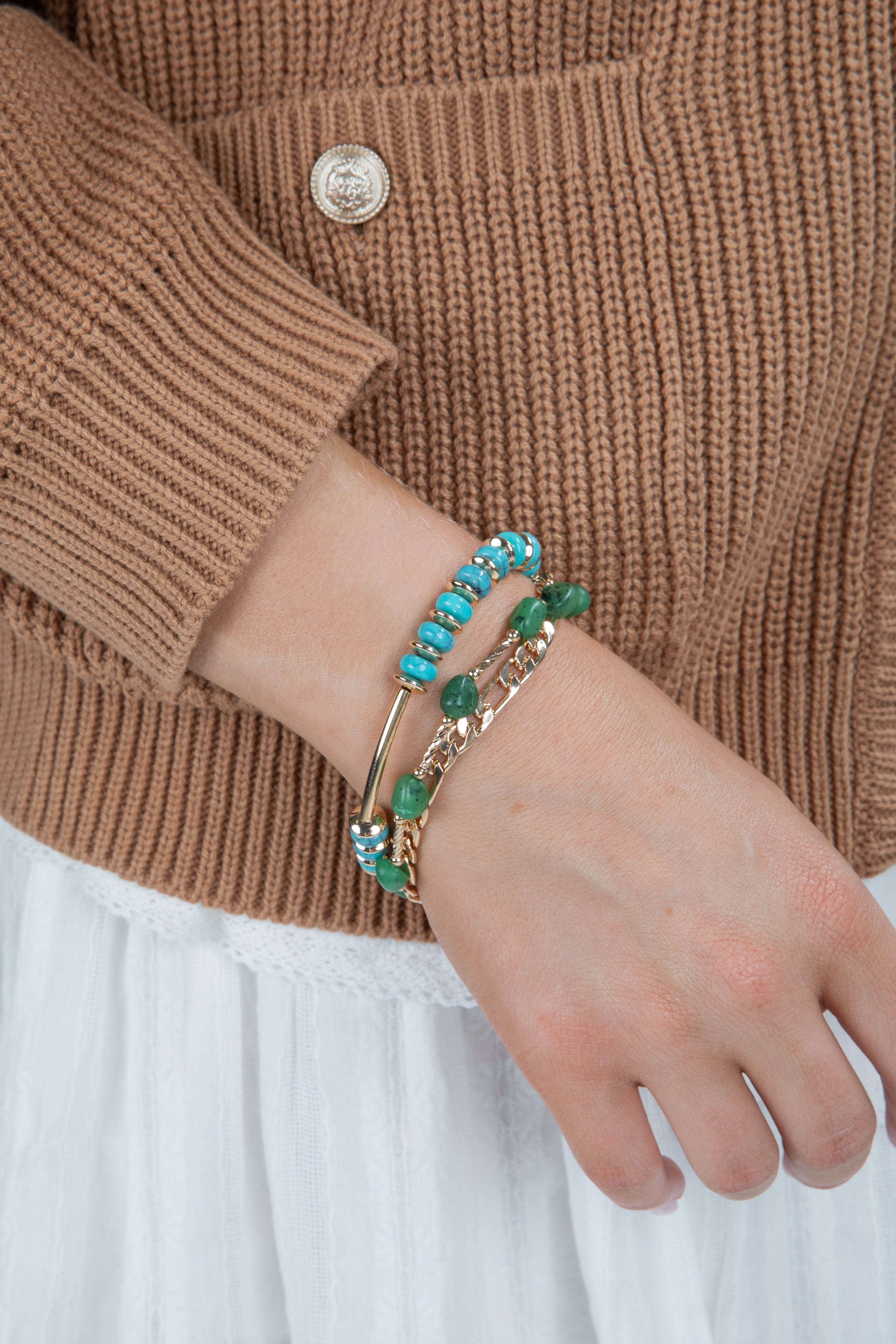 Close-up of a hand wearing two bracelets with turquoise stones on a brown sweater background