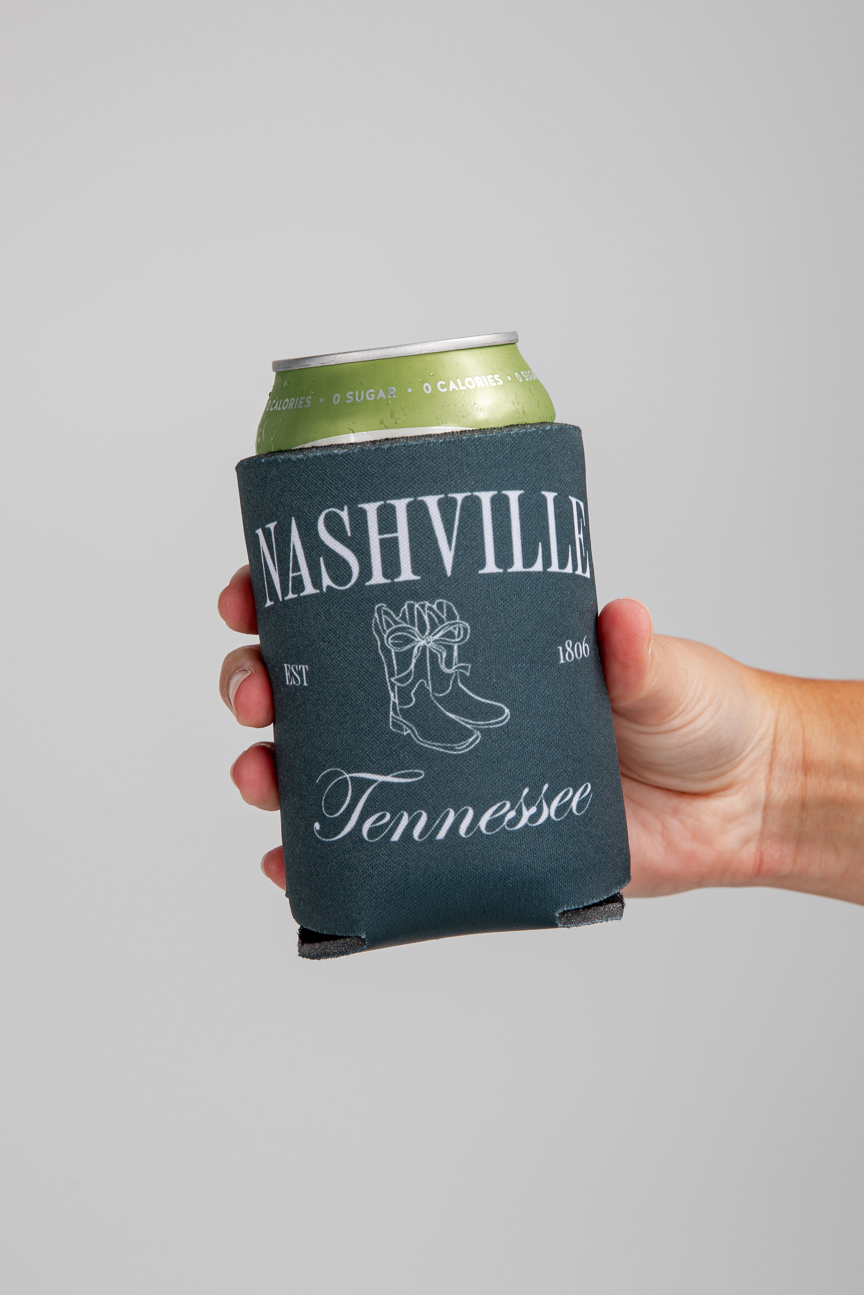 Hand holding a can with a Nashville, Tennessee koozie against a gray background