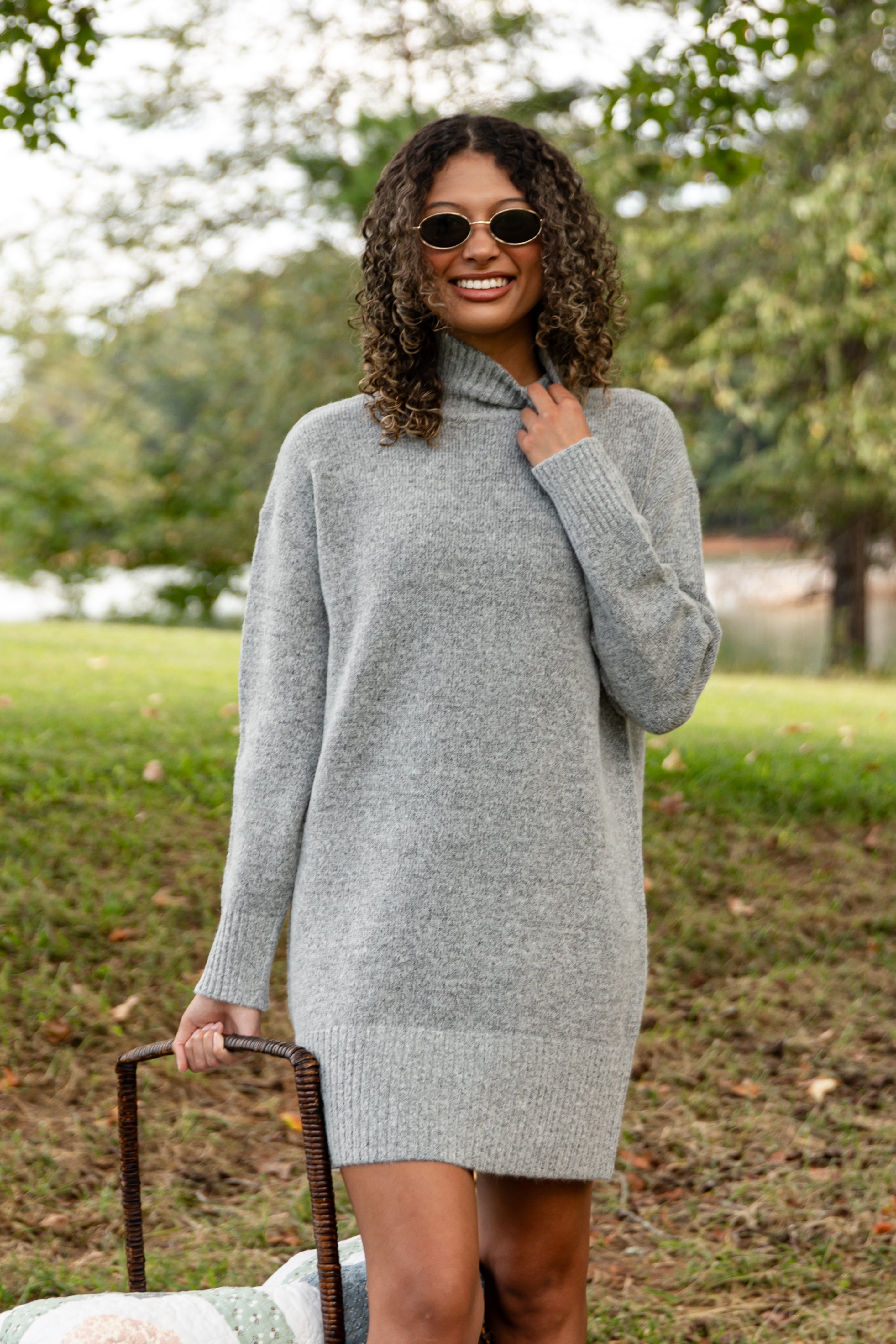 Woman wearing a gray sweater dress outdoors with trees in the background