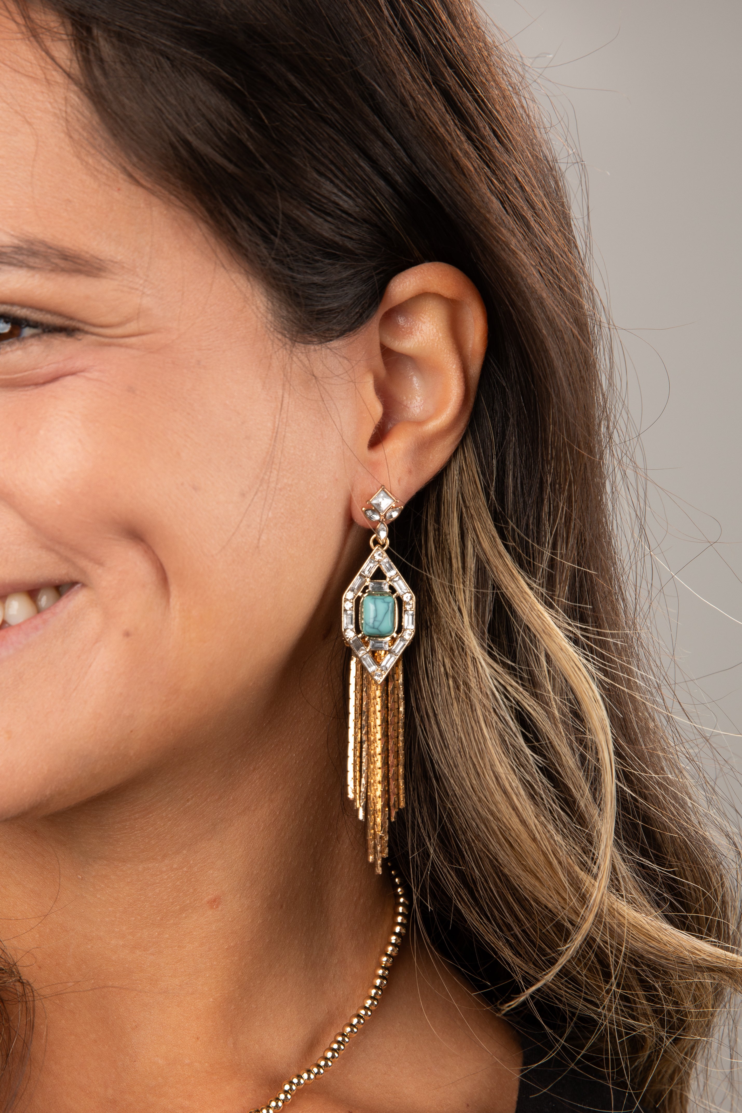 Close-up of a woman wearing a gold earring with a turquoise gemstone.