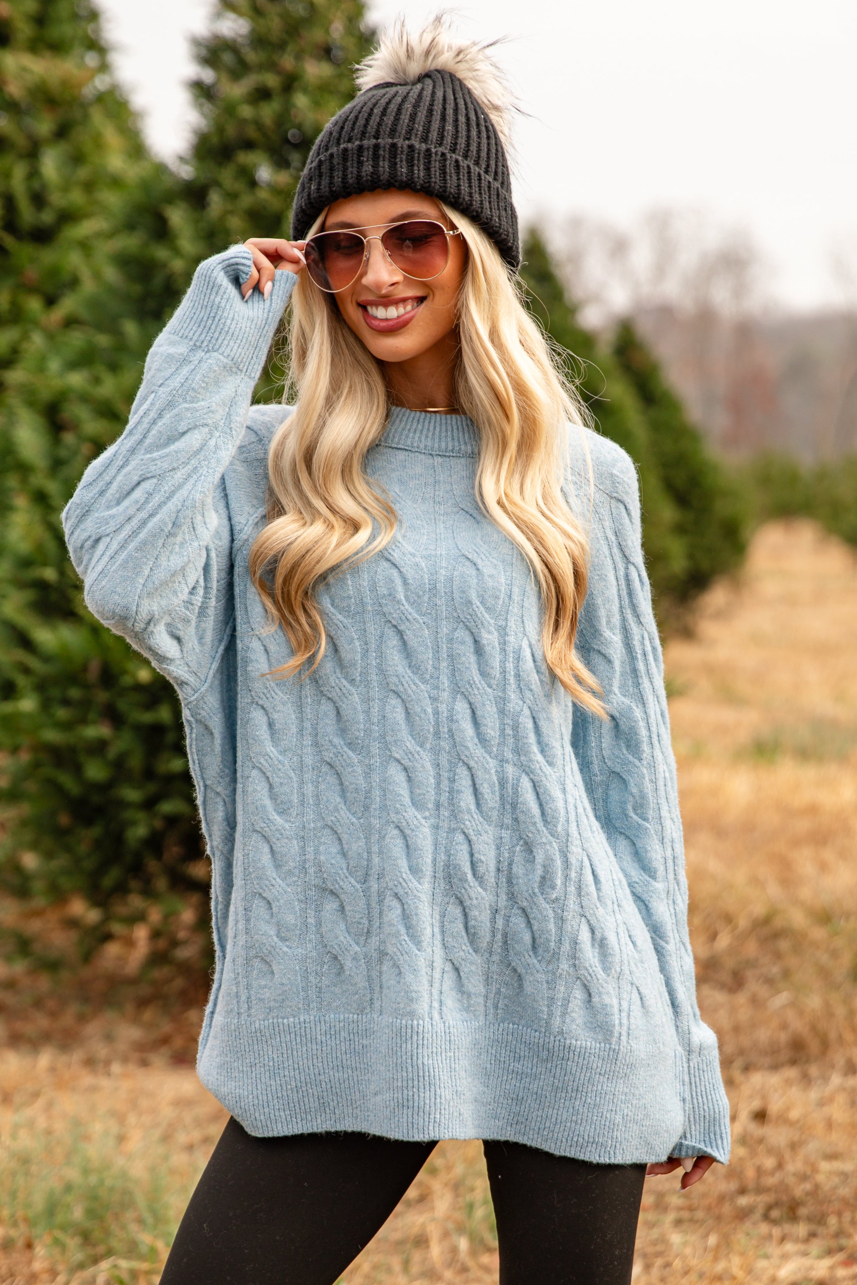 Woman wearing a light blue cable knit sweater and black beanie in a forest setting