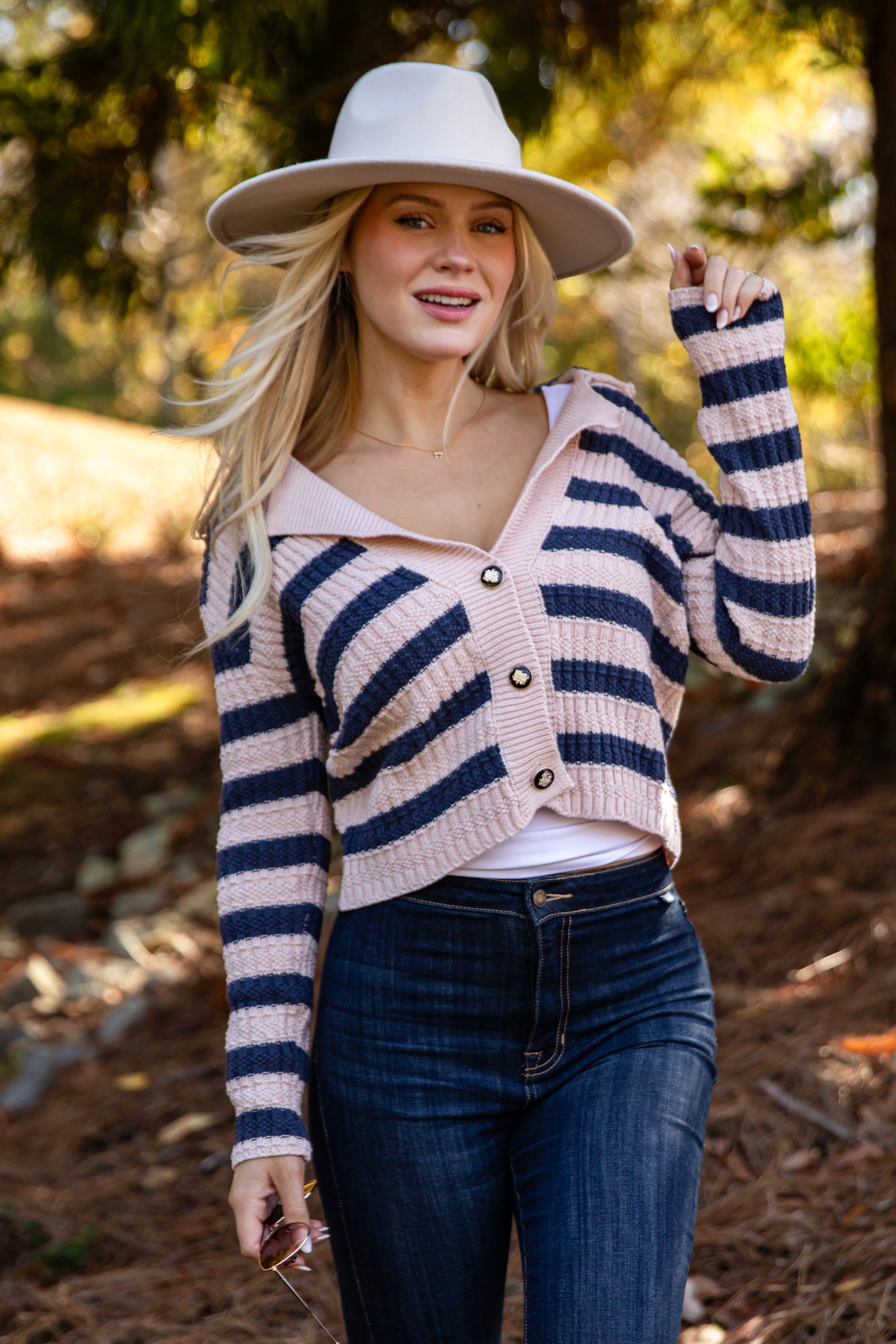 Woman wearing a striped cardigan, white hat, and blue jeans outdoors.