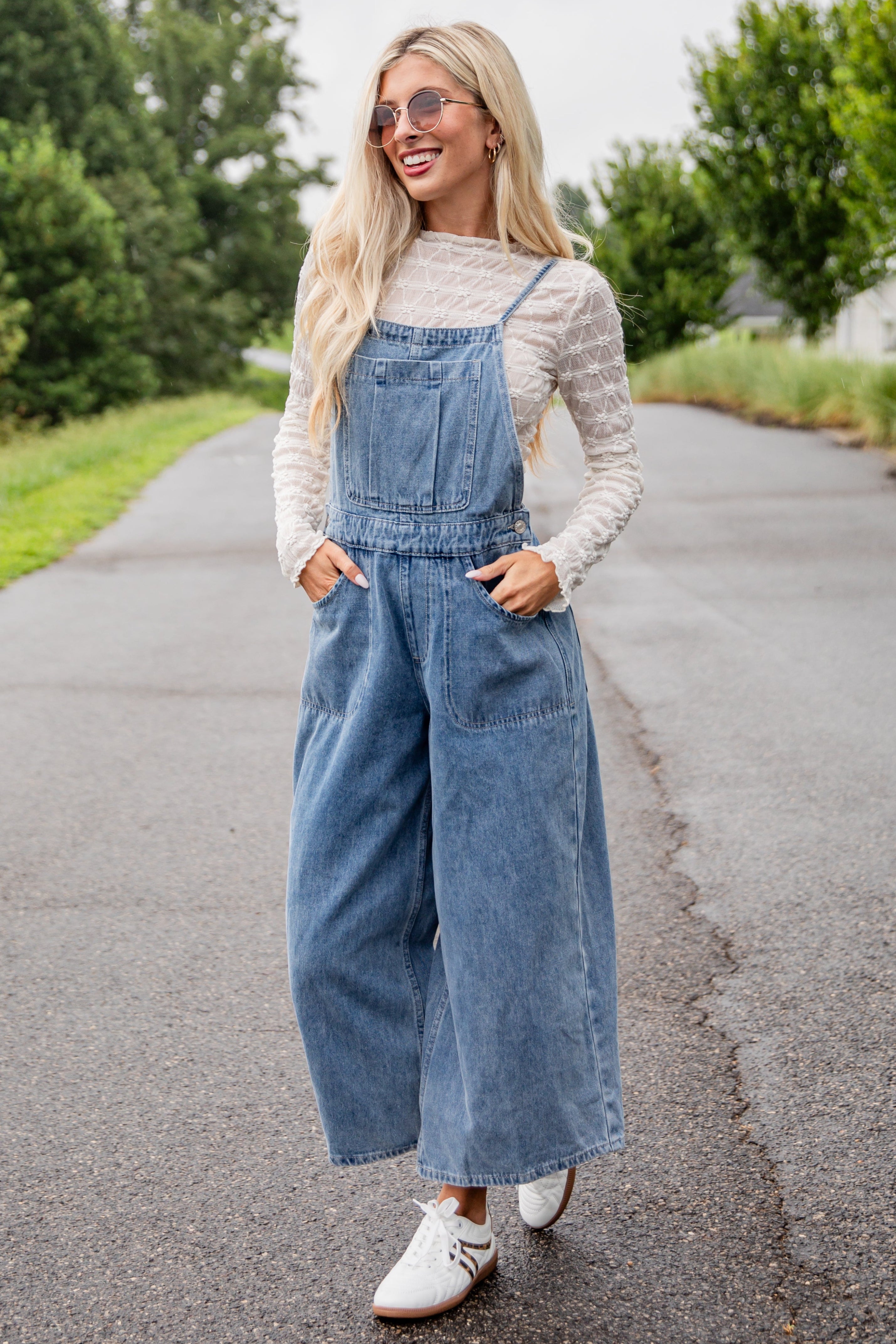 Woman wearing a denim overalls outfit on a road with trees in the background