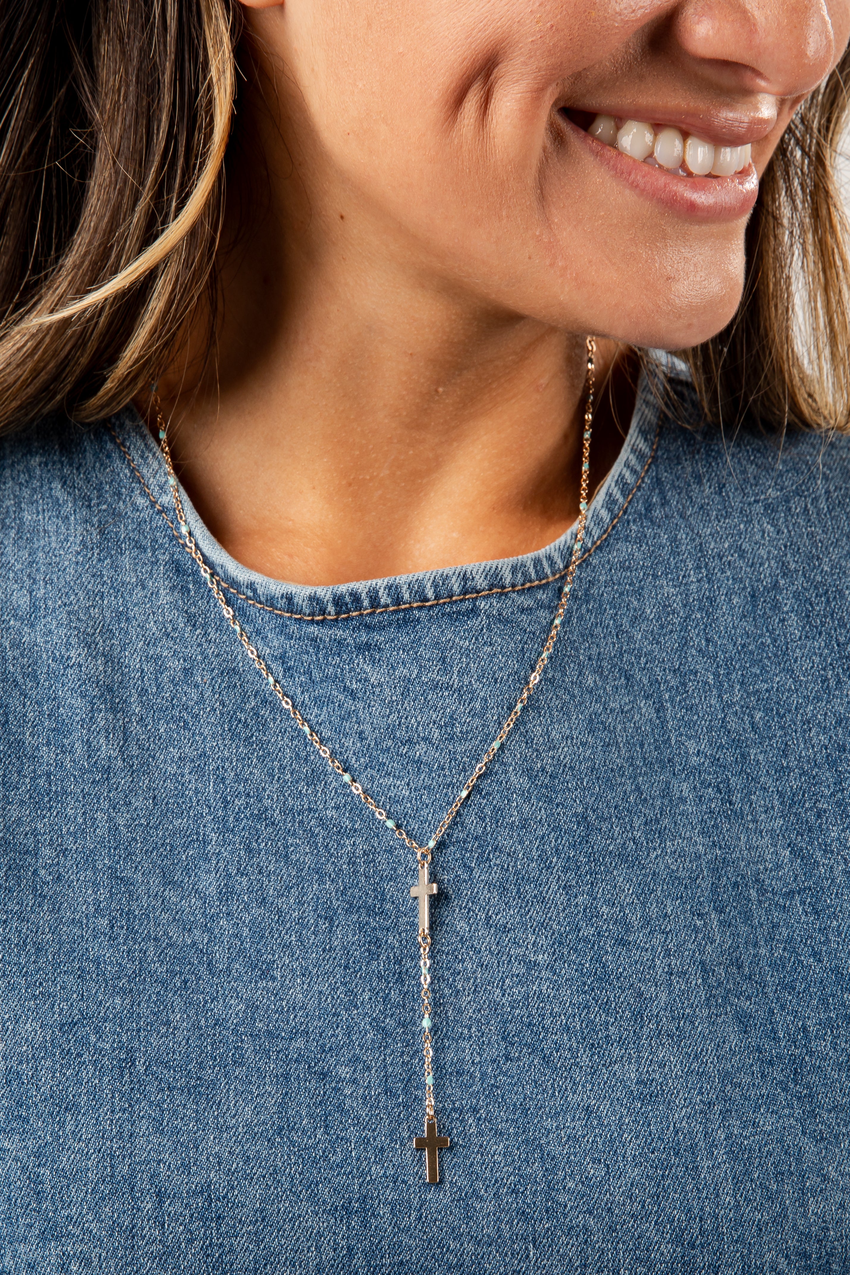 Close-up of a person wearing a necklace with a cross pendant, set against a denim background.
