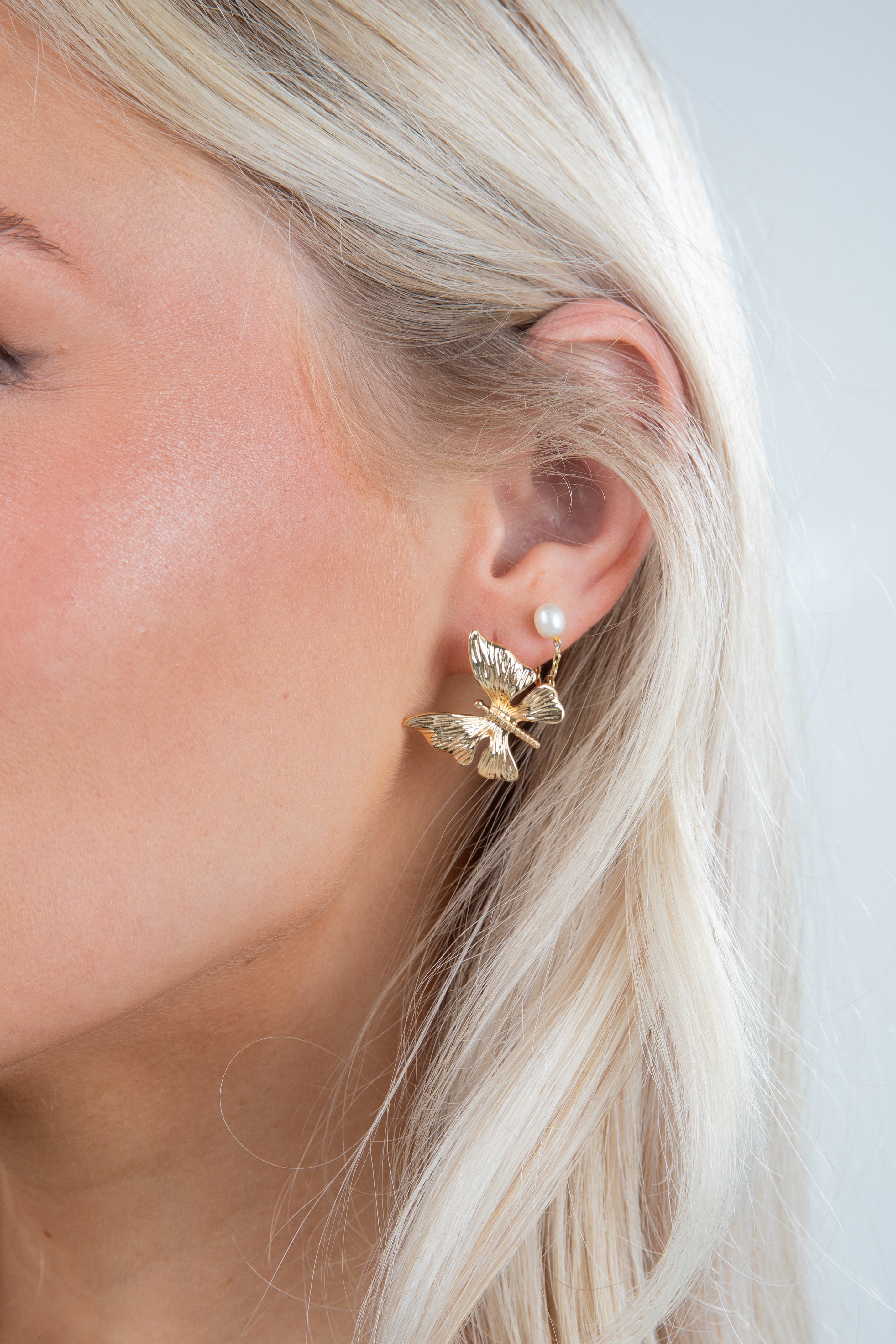 Close-up of a person wearing a gold butterfly earring with a pearl accent.