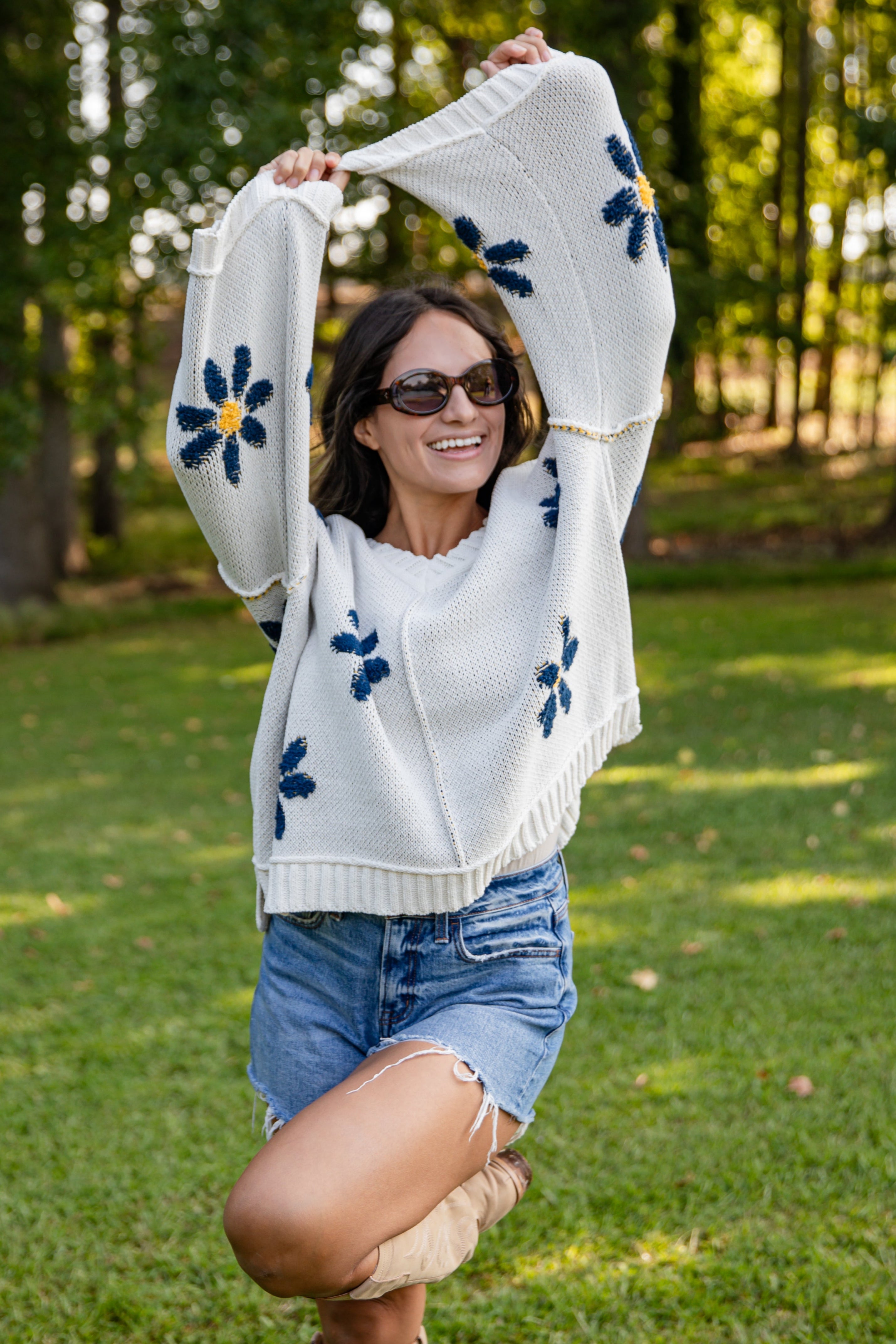 Woman wearing a white sweater with blue floral patterns in an outdoor setting