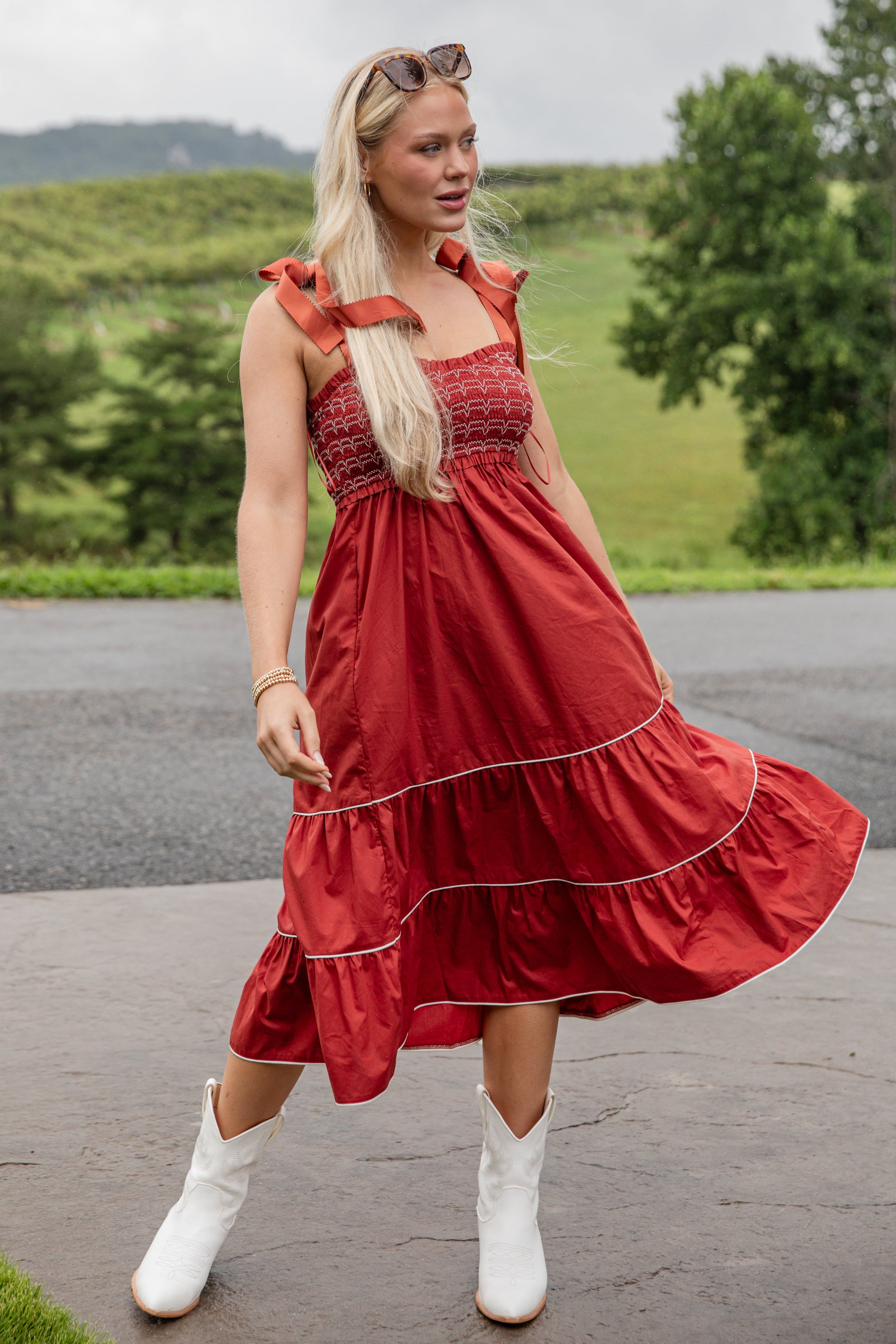 Woman in a red dress with white boots standing outdoors with greenery in the background