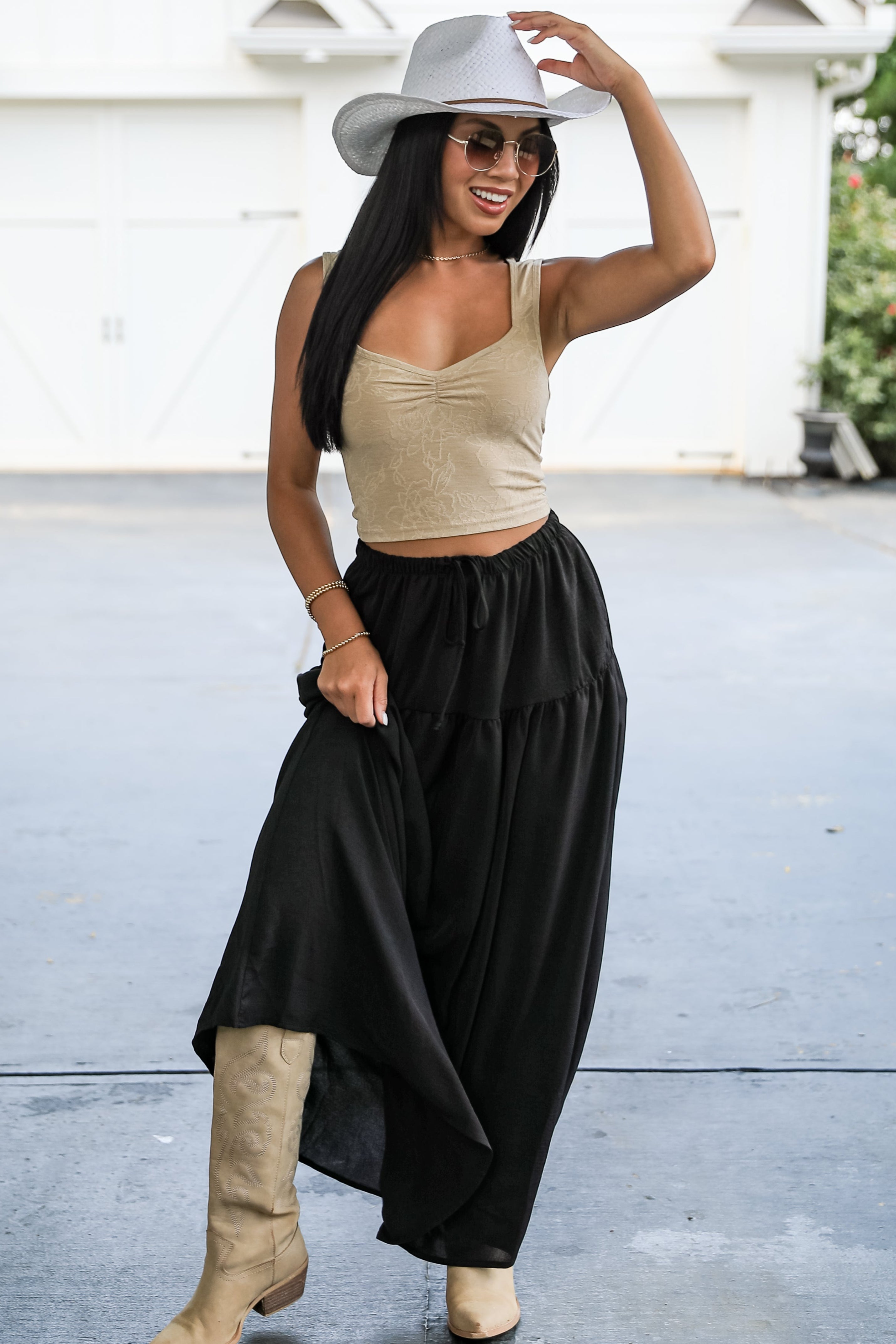 Woman wearing a beige top, black wide-leg pants, and a white hat in an outdoor setting.