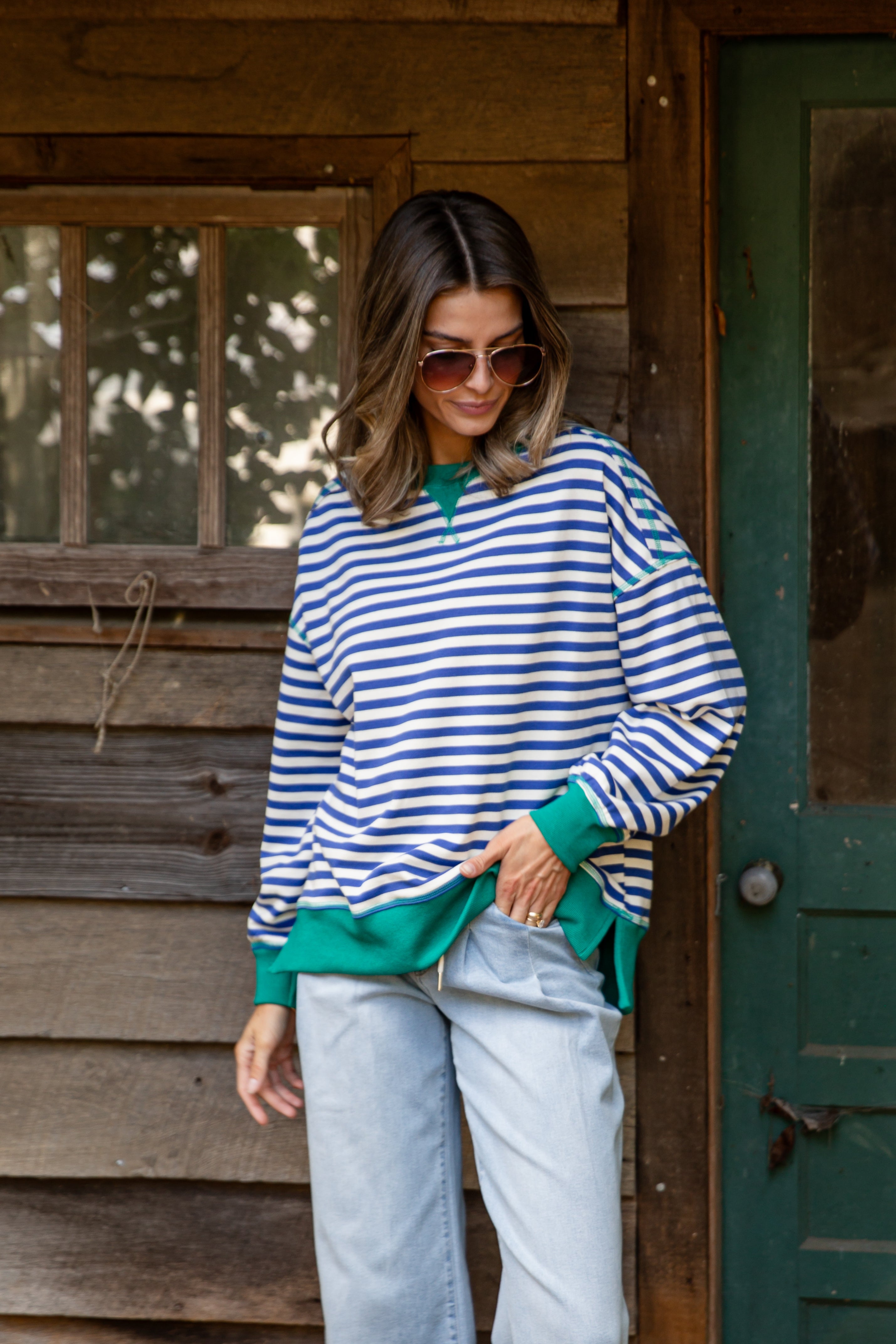 Woman wearing a blue and white striped sweater with green trim standing in front of a wooden cabin.