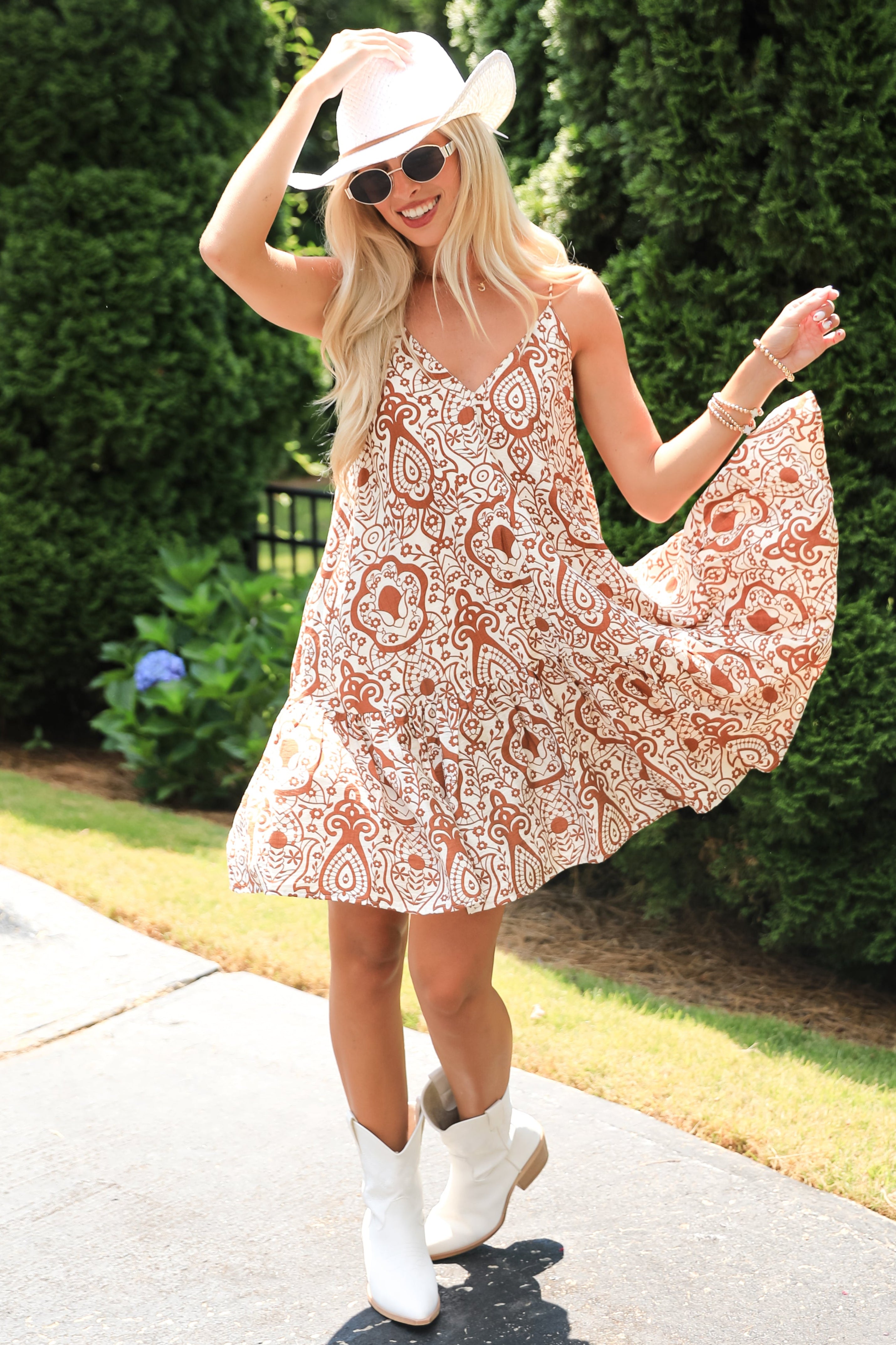 Woman in a floral dress and white cowboy boots posing outdoors.
