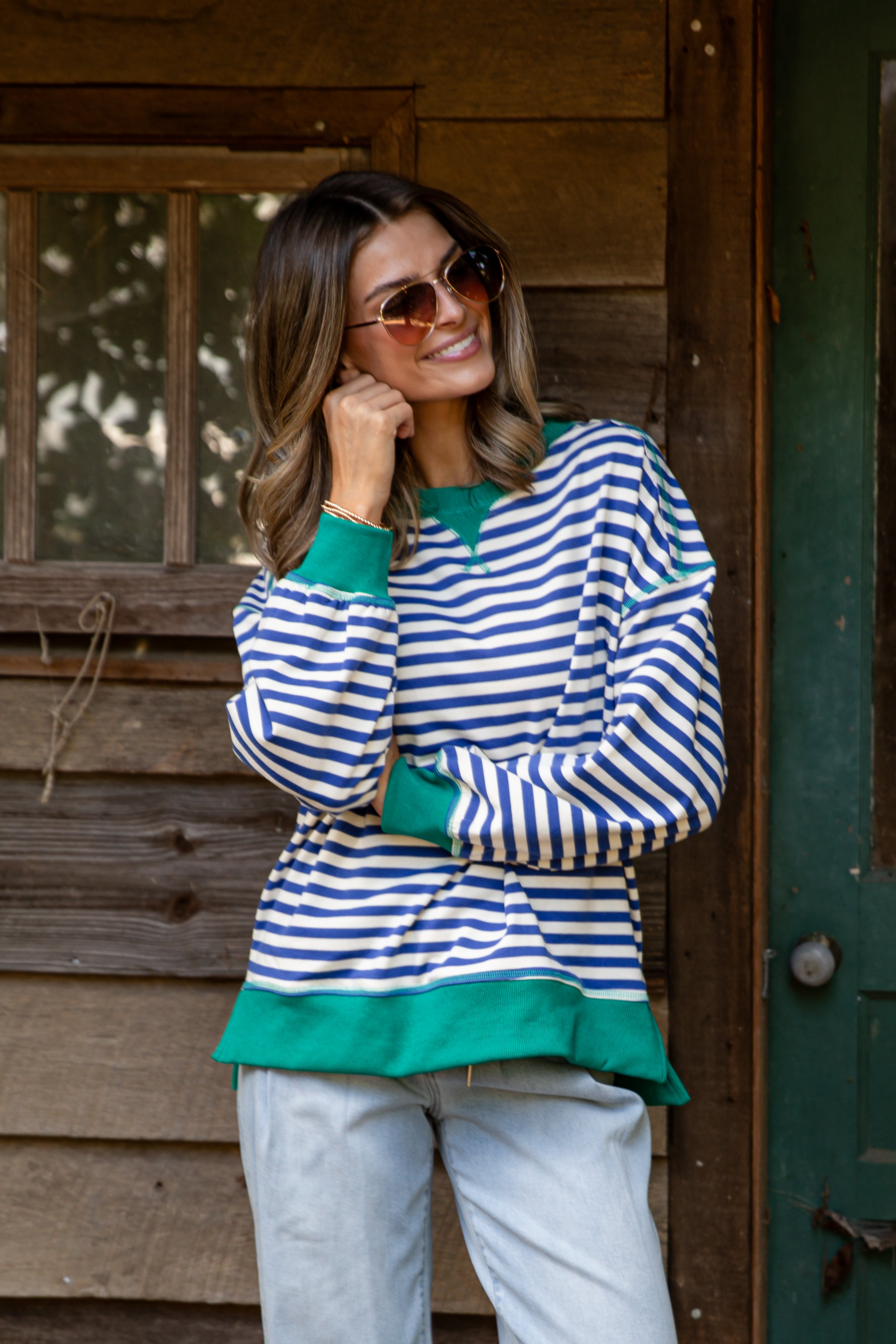Woman wearing a striped sweater with green accents standing in front of a wooden cabin.