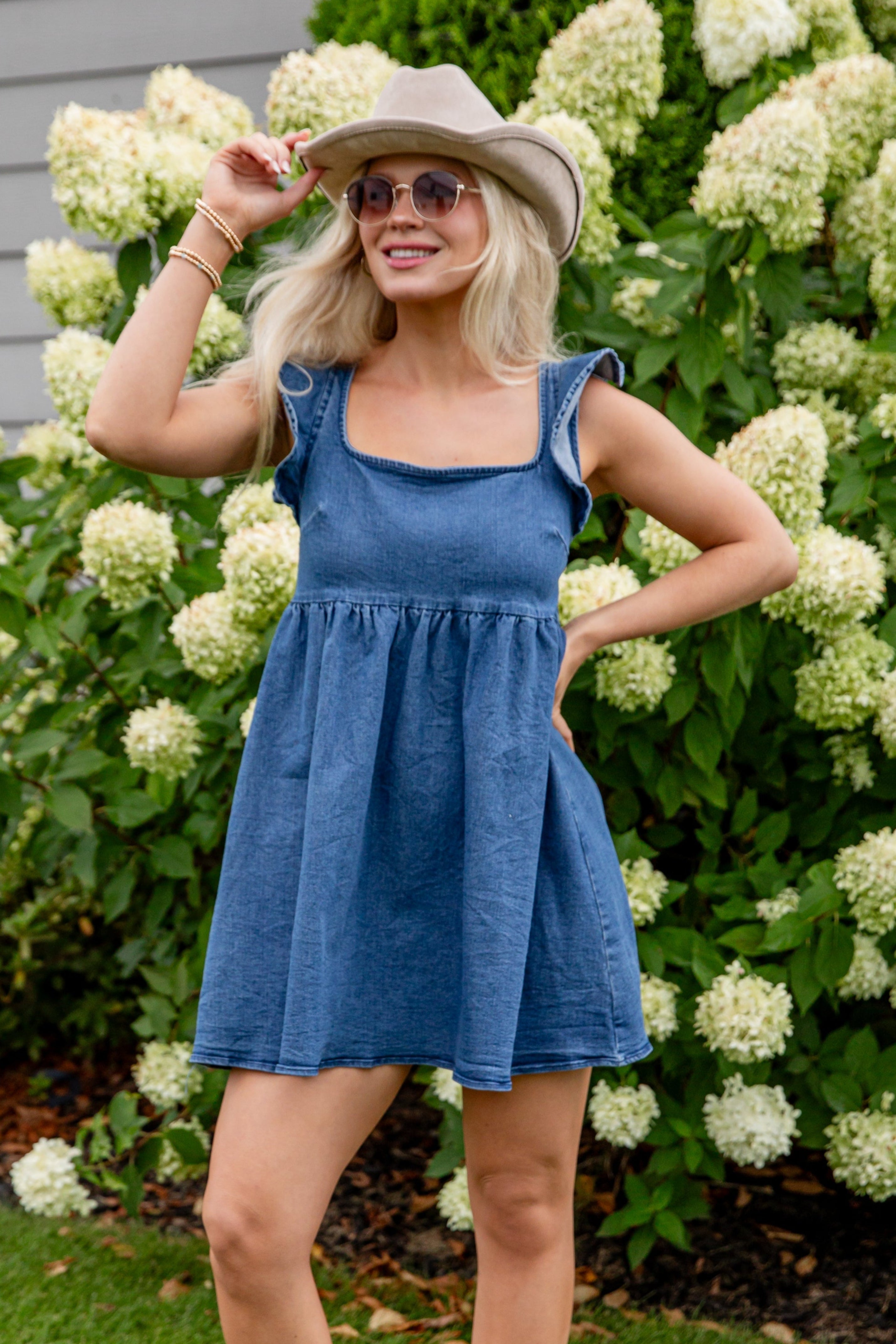 Woman in a blue dress and white boots standing in front of white flowers.