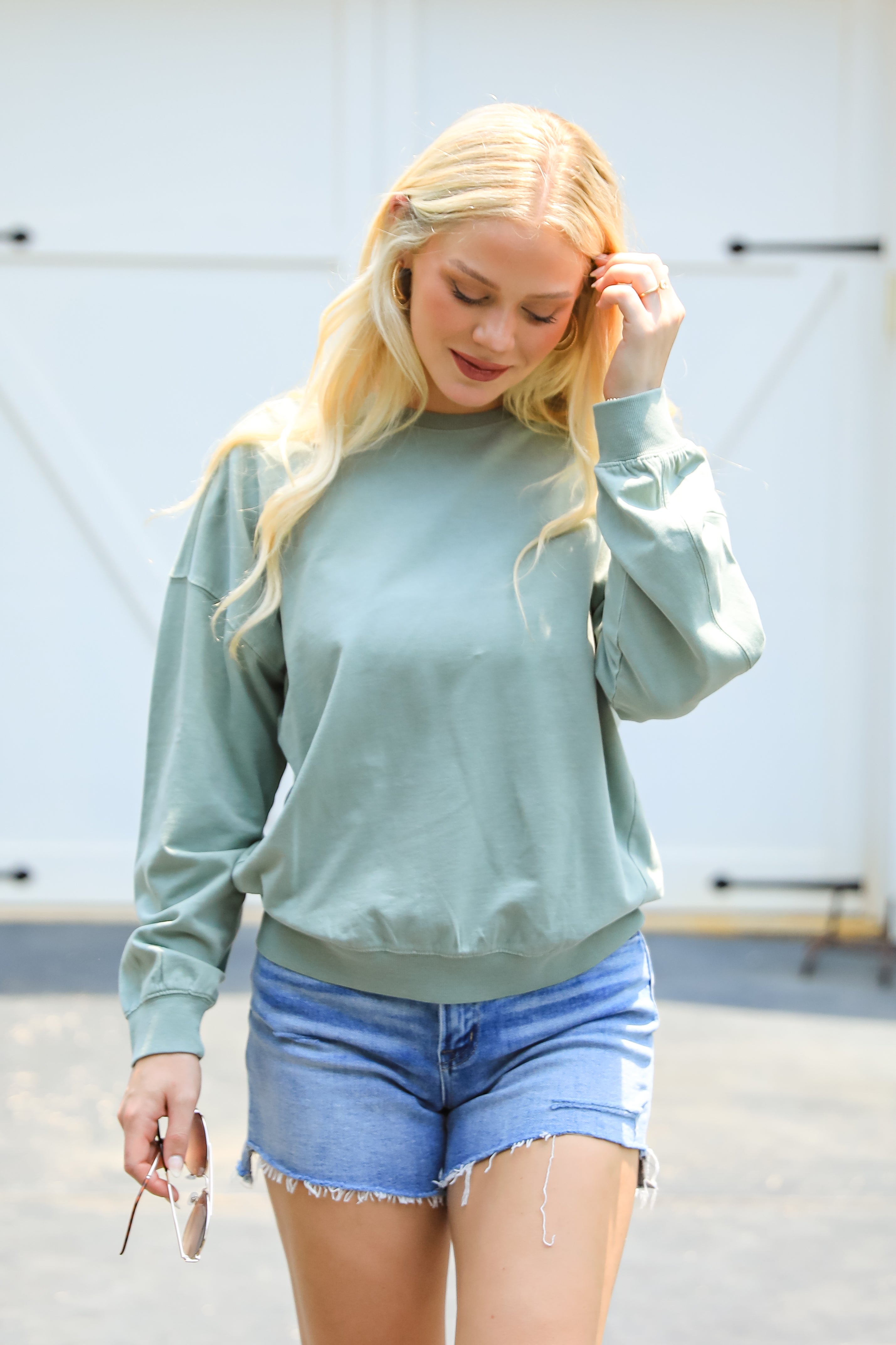 Woman wearing a light blue sweatshirt and denim shorts outdoors.