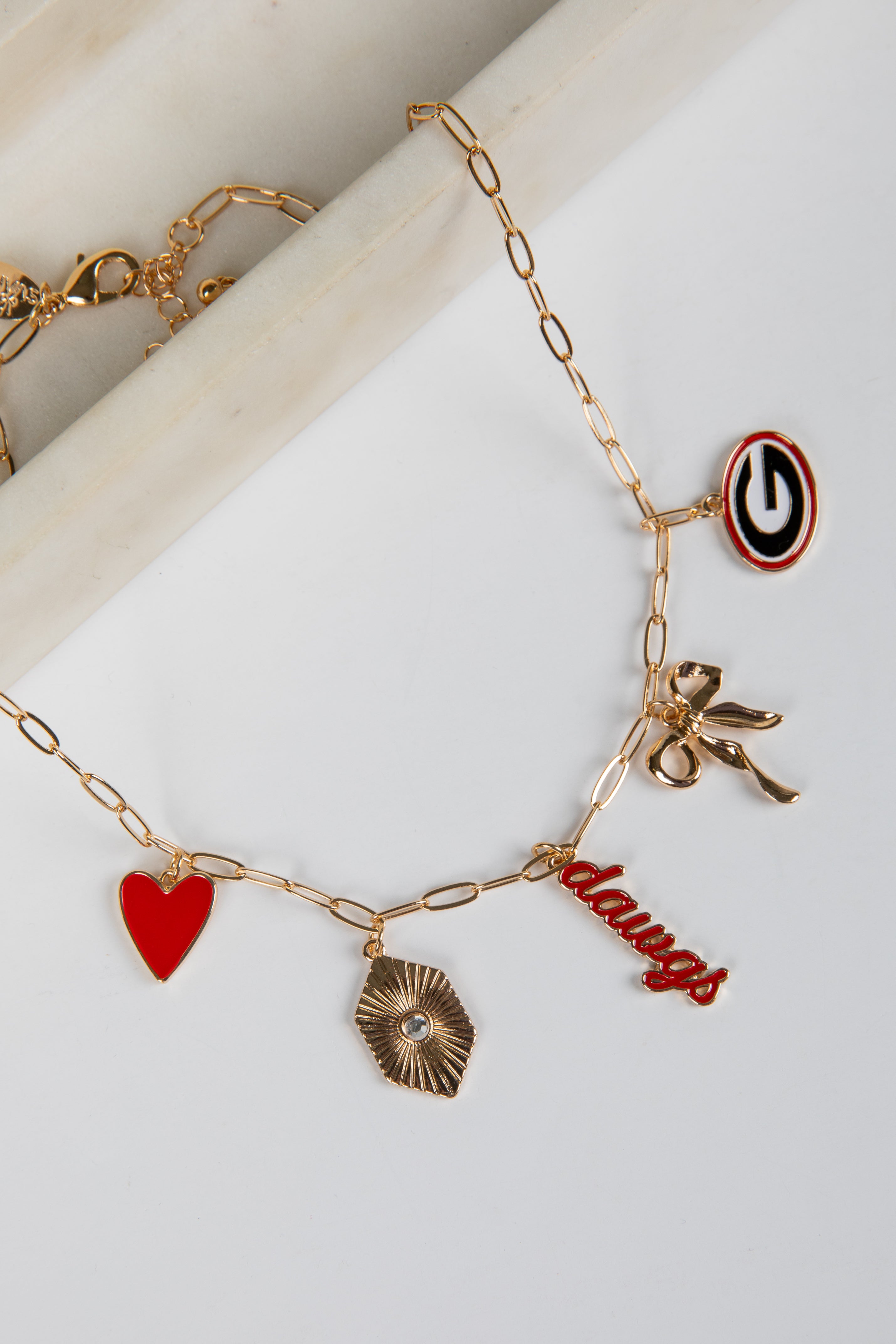 Gold bracelet with various charms including a heart, bow, and word charm on a white surface.