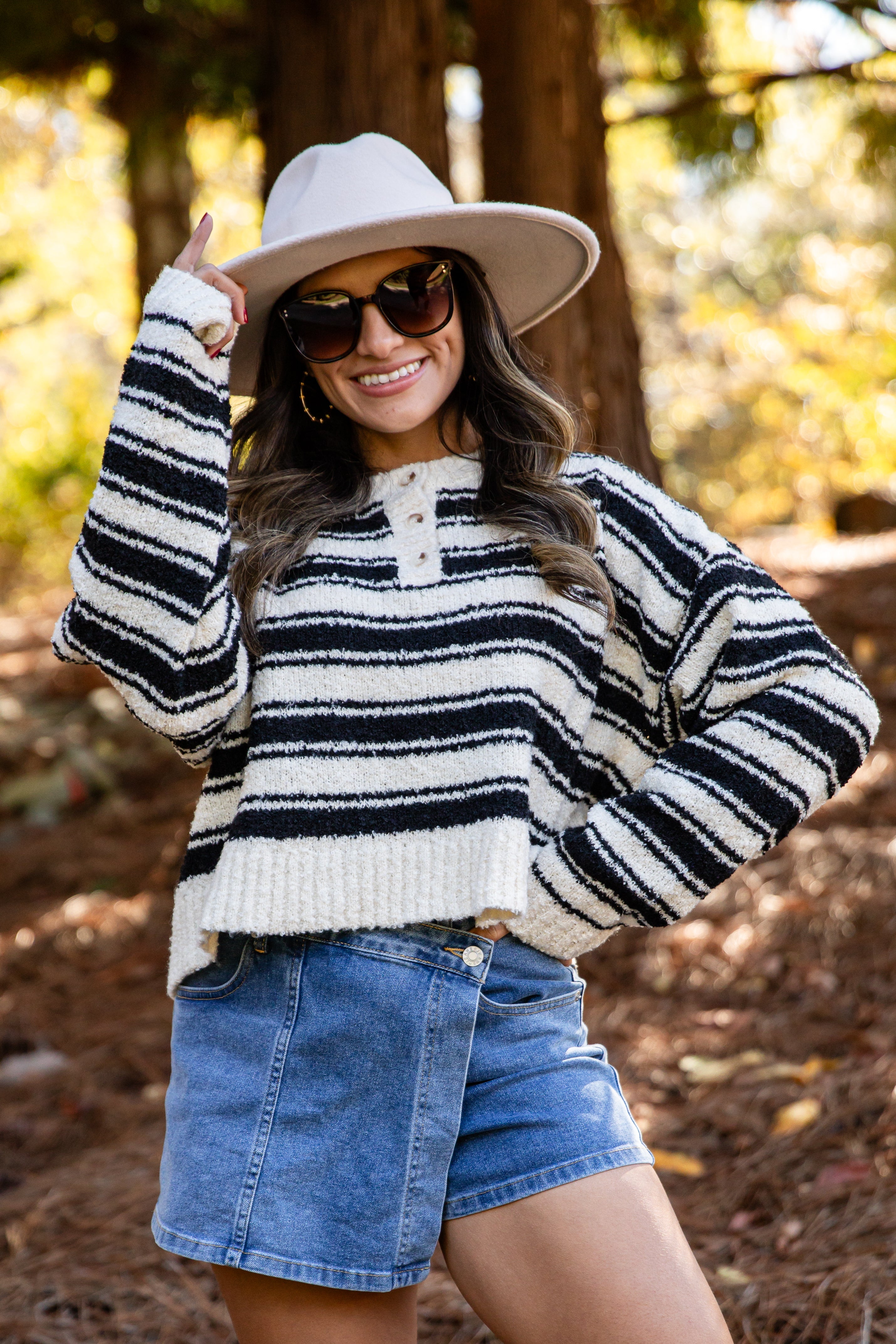 Woman wearing a striped sweater and denim shorts in a forest setting