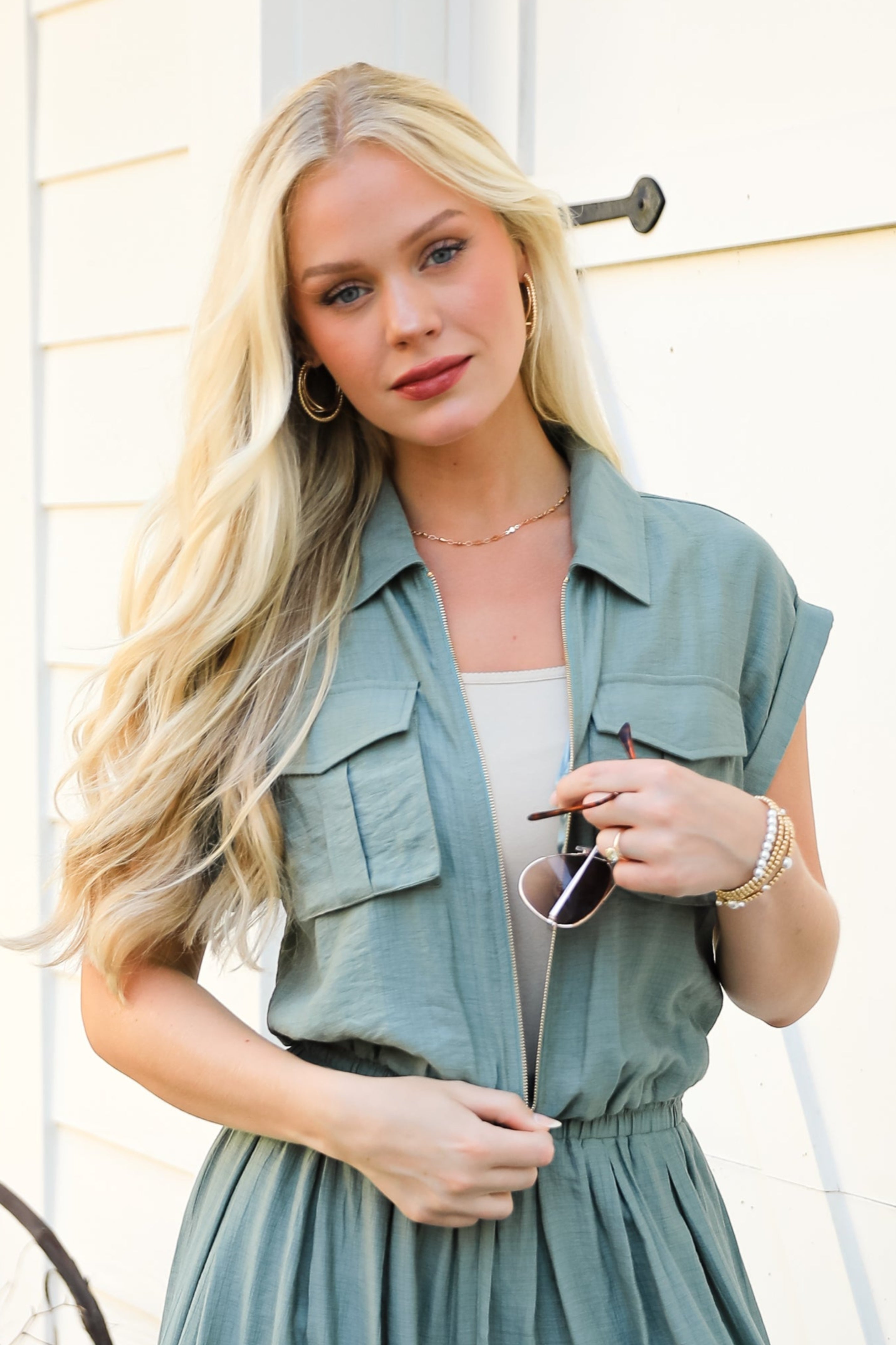 Woman wearing a teal jumpsuit standing in front of a white door.