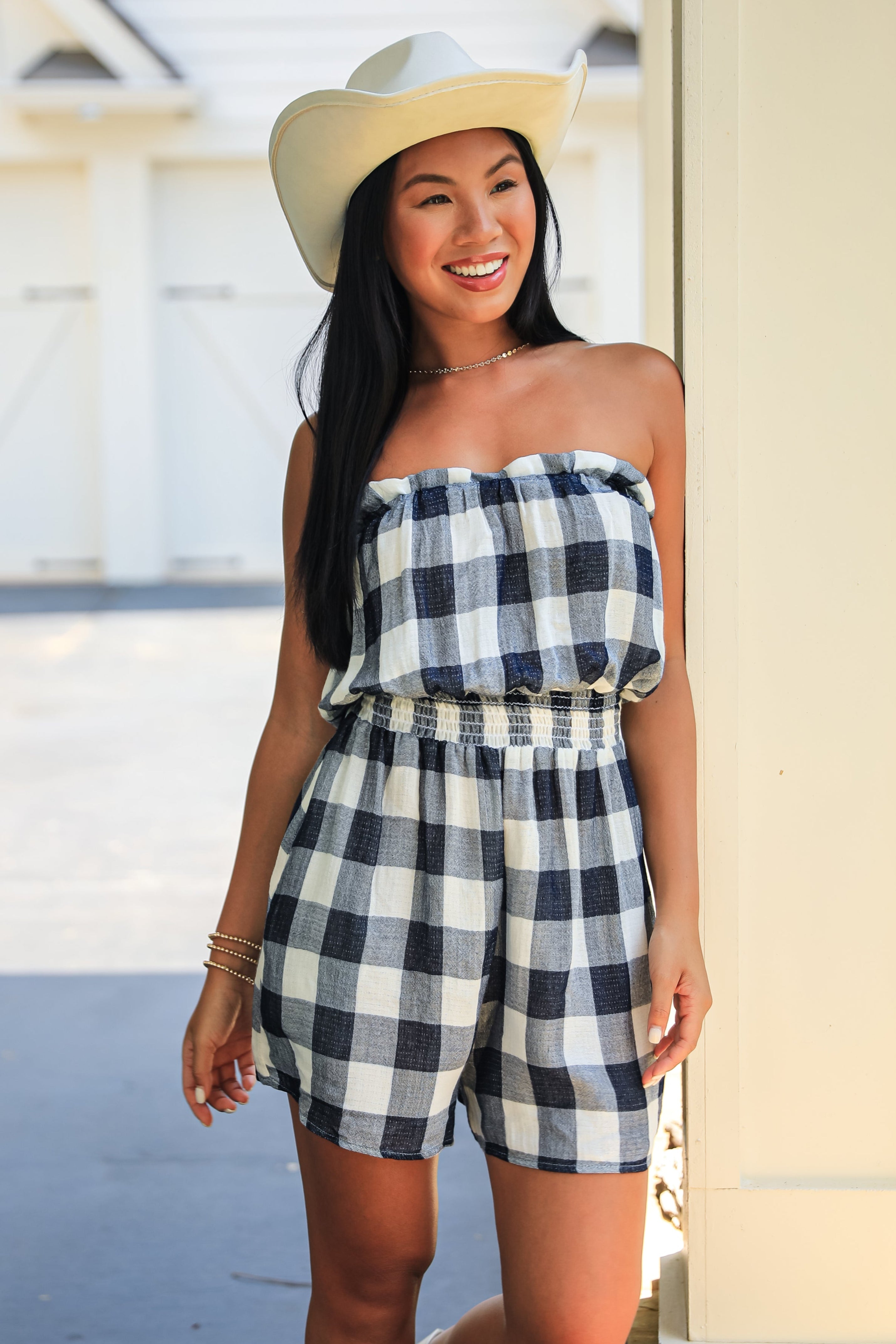 Woman wearing a checkered strapless romper and hat outdoors.