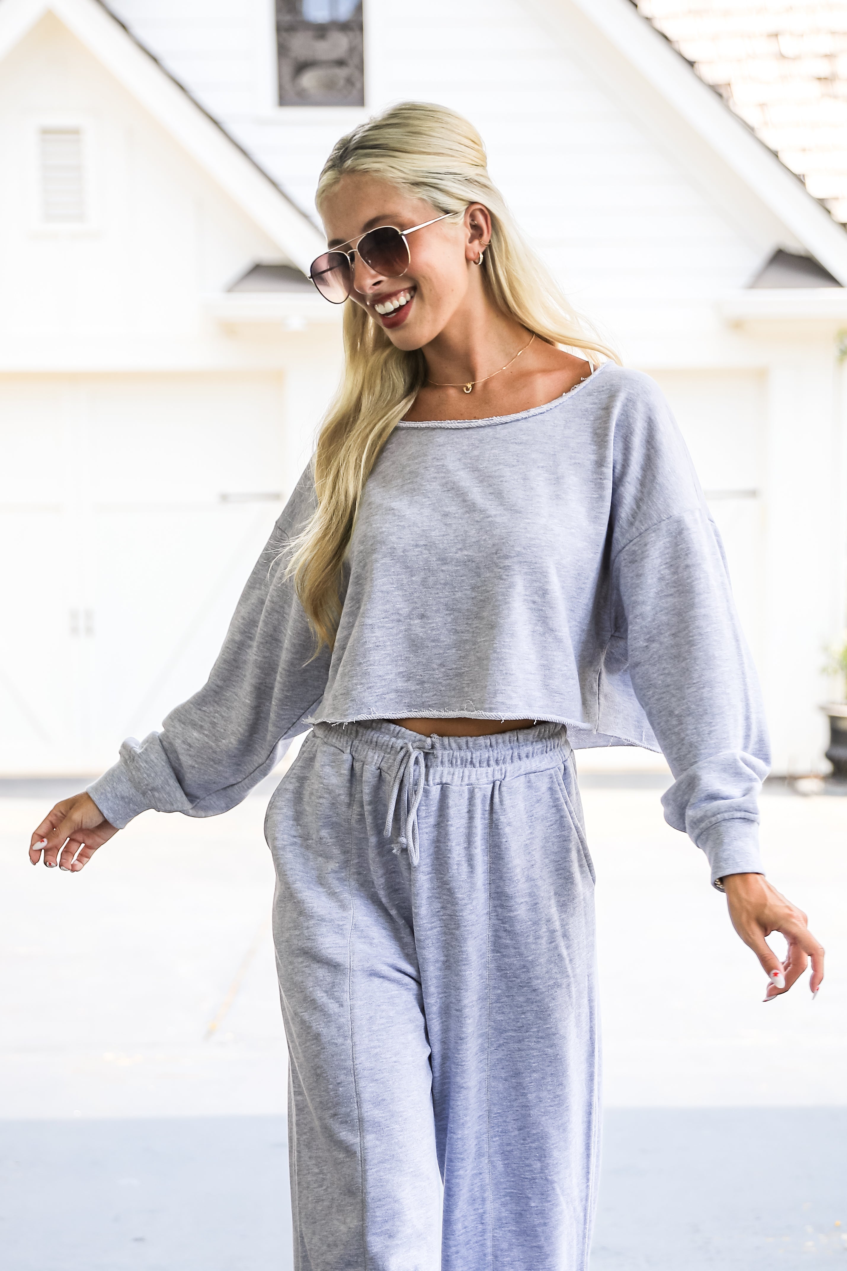Woman wearing a gray sweatshirt and pants with sunglasses, standing indoors.