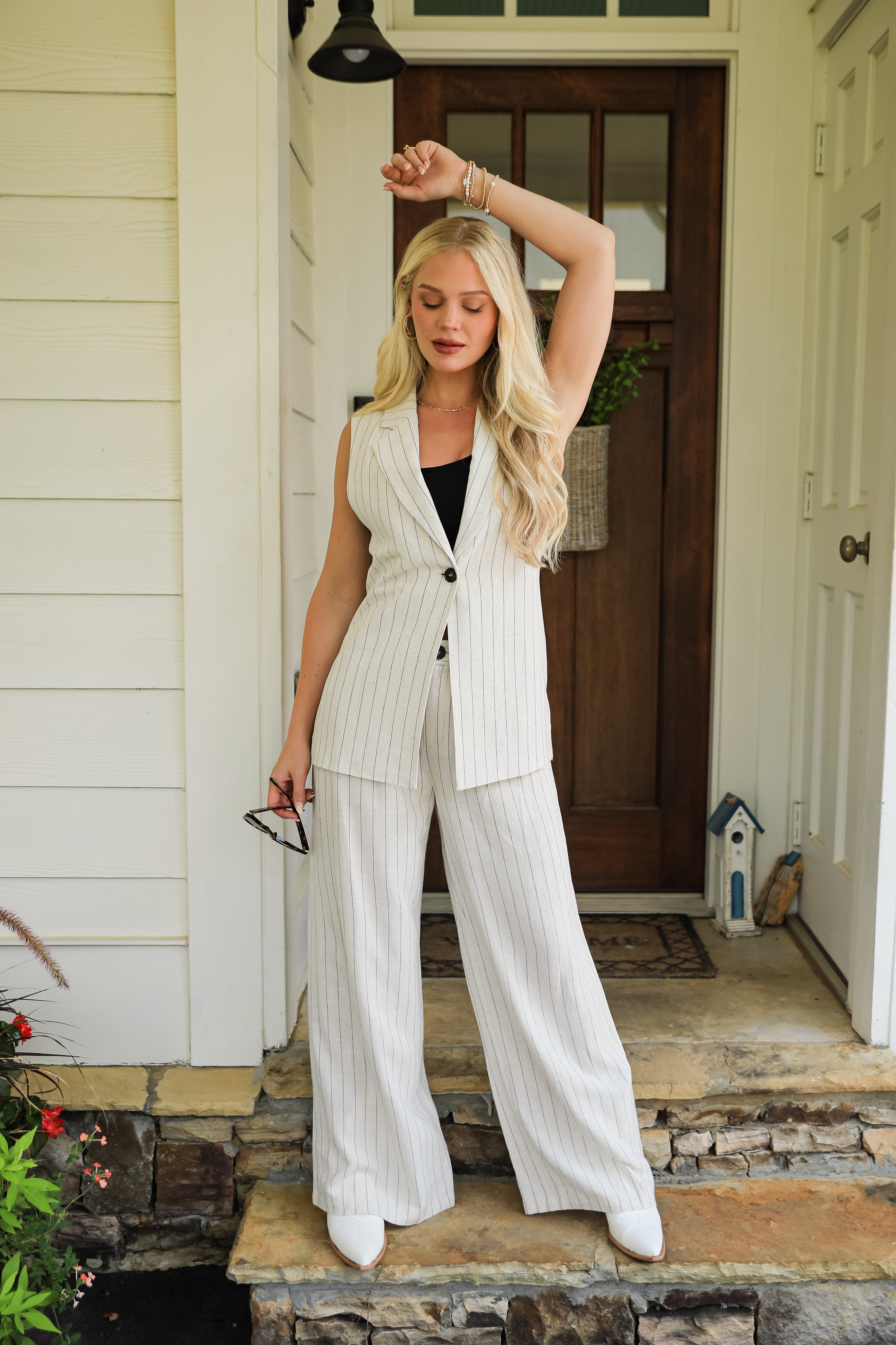 Woman in a white pinstripe suit standing on a porch.