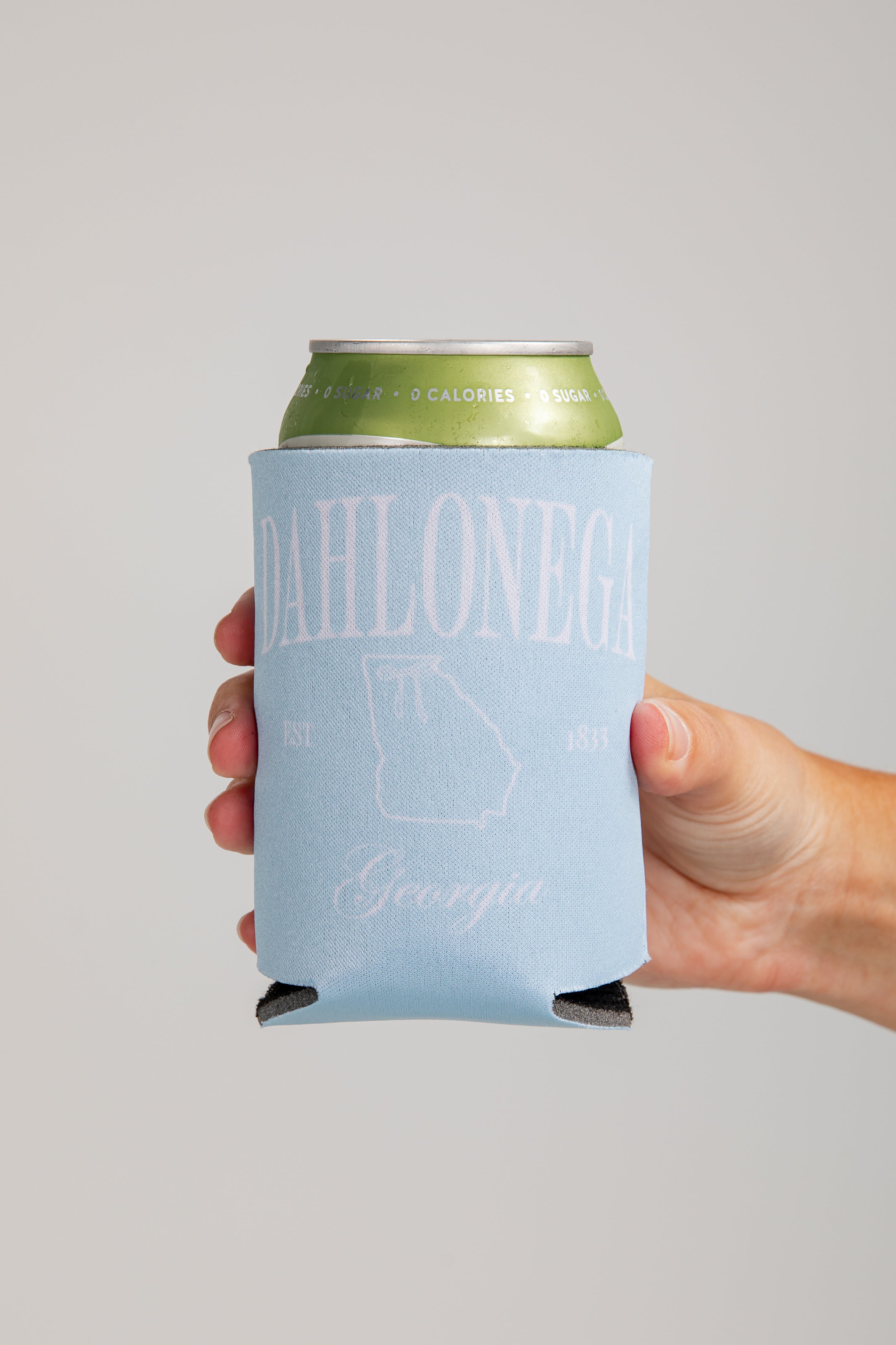 Hand holding a can with a blue sleeve featuring text and a map on a gray background