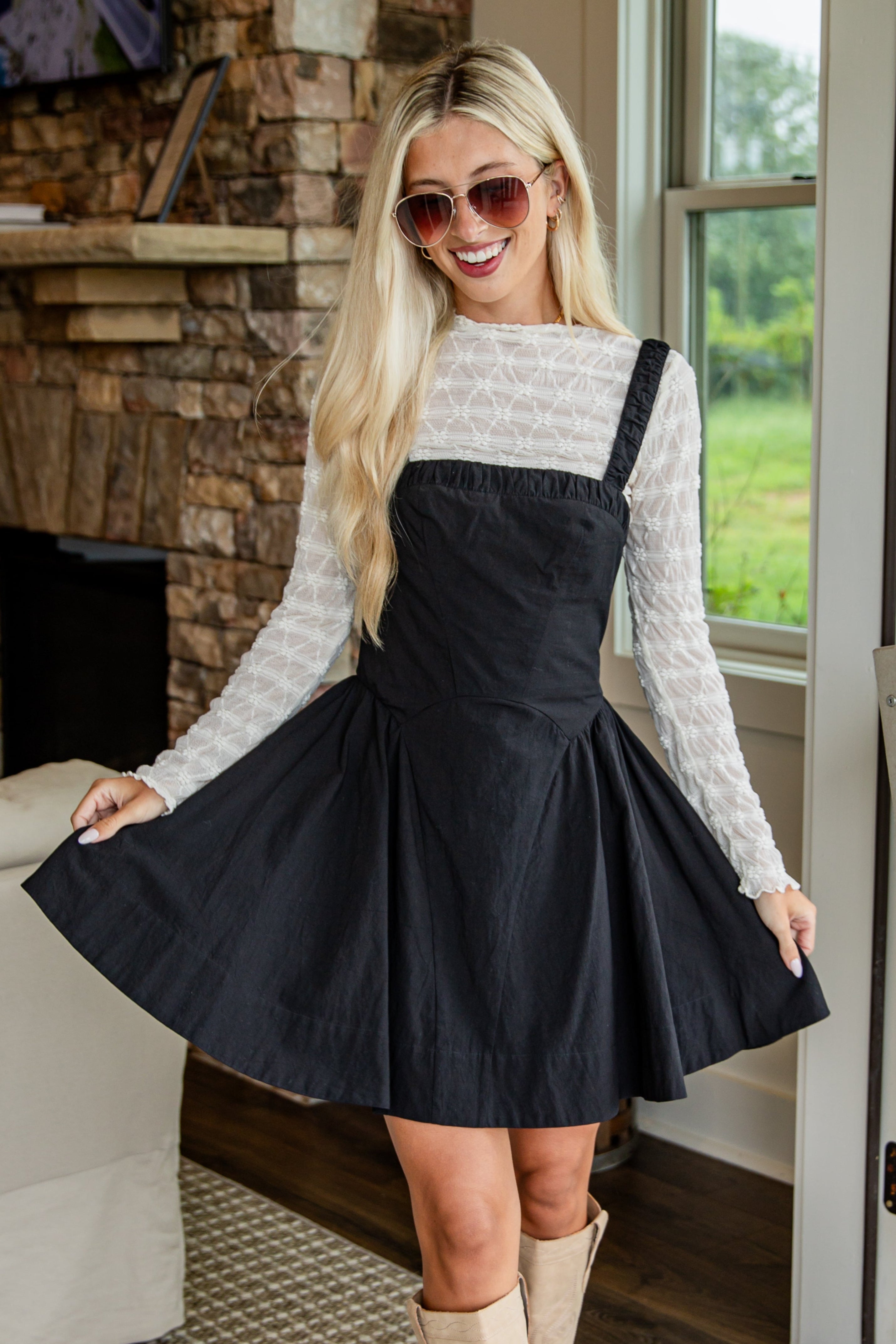 Woman in a black dress and beige boots standing on a porch.