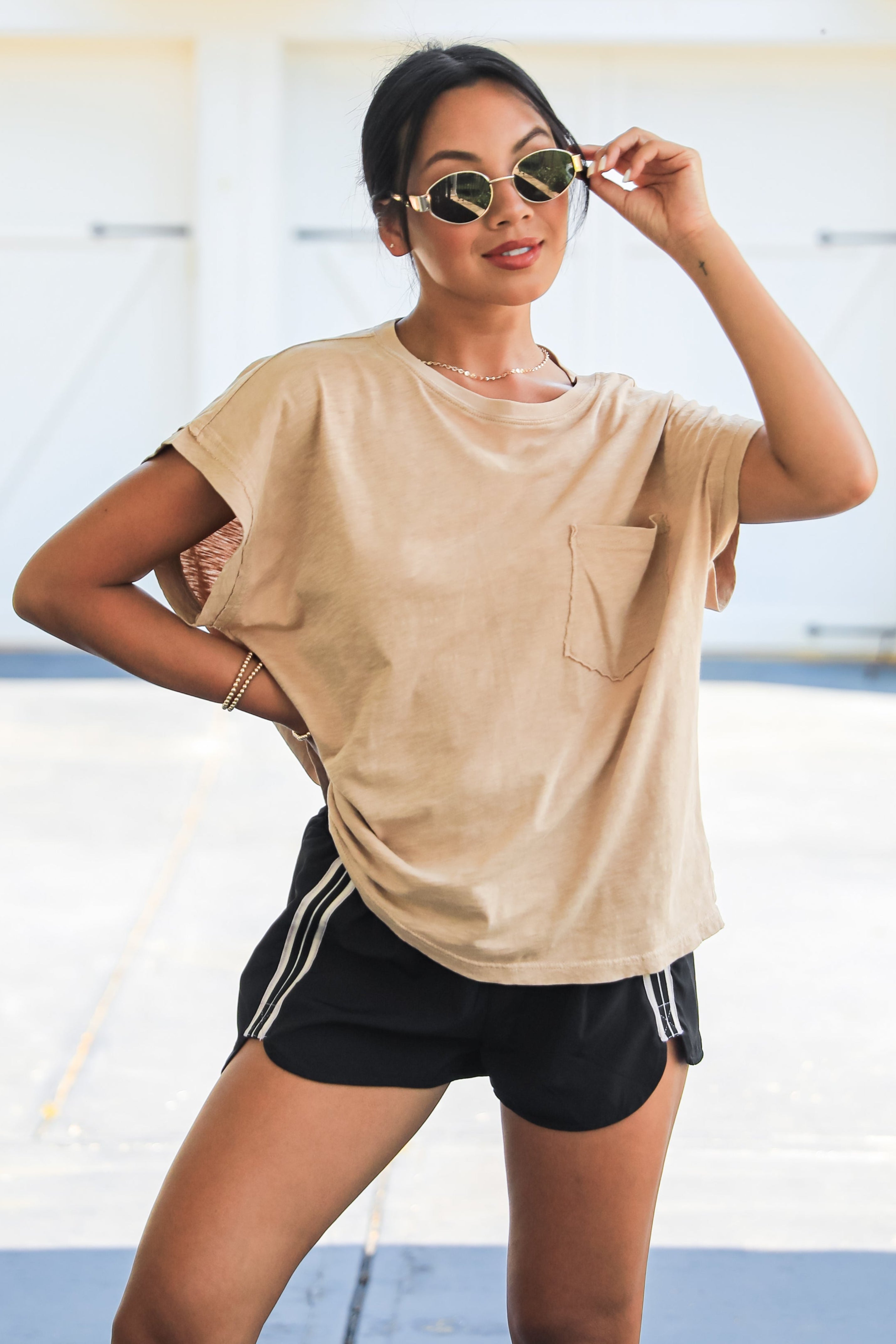 Woman wearing a beige t-shirt and black shorts with white stripes outdoors.