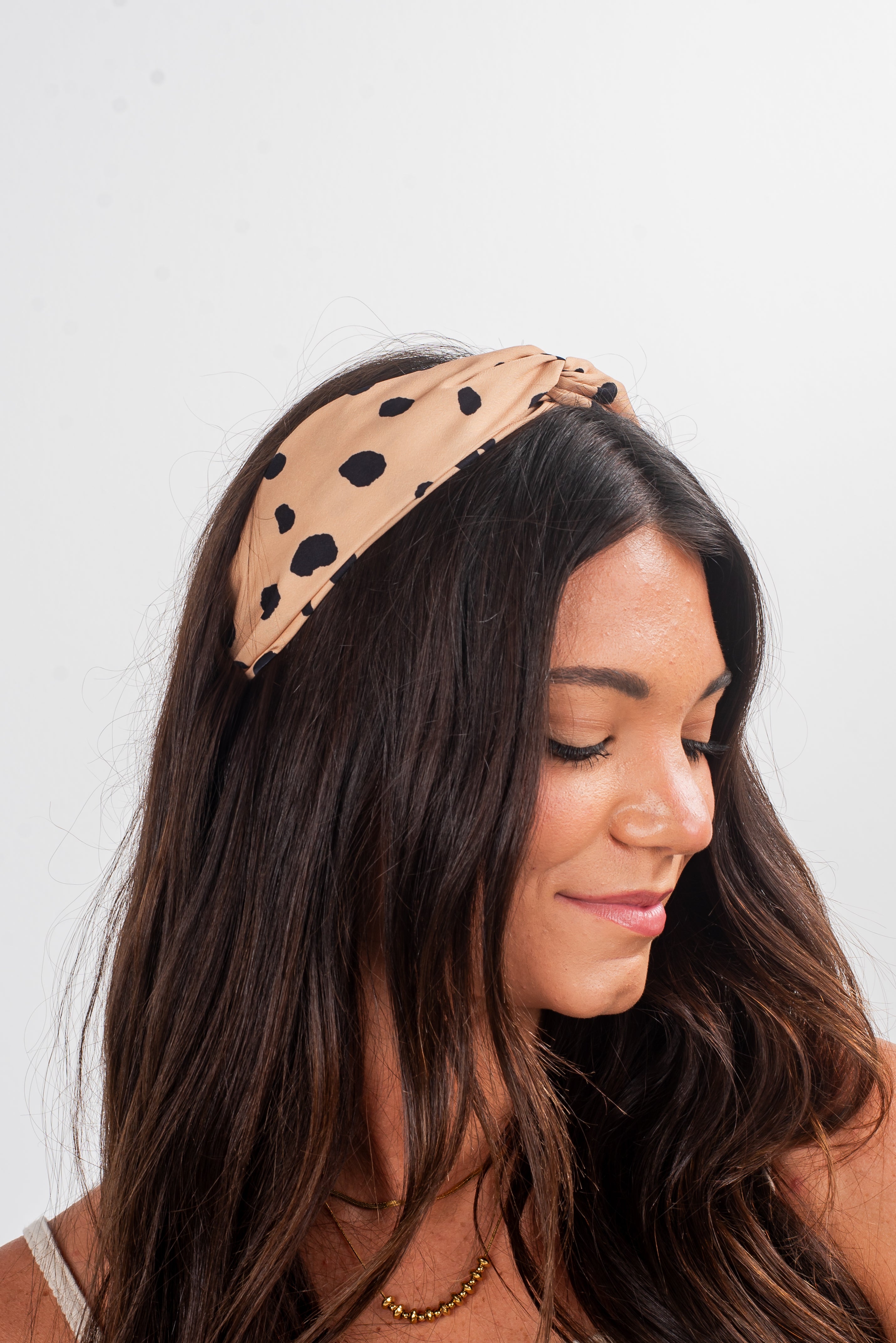 Woman wearing a beige headband with black polka dots on a white background