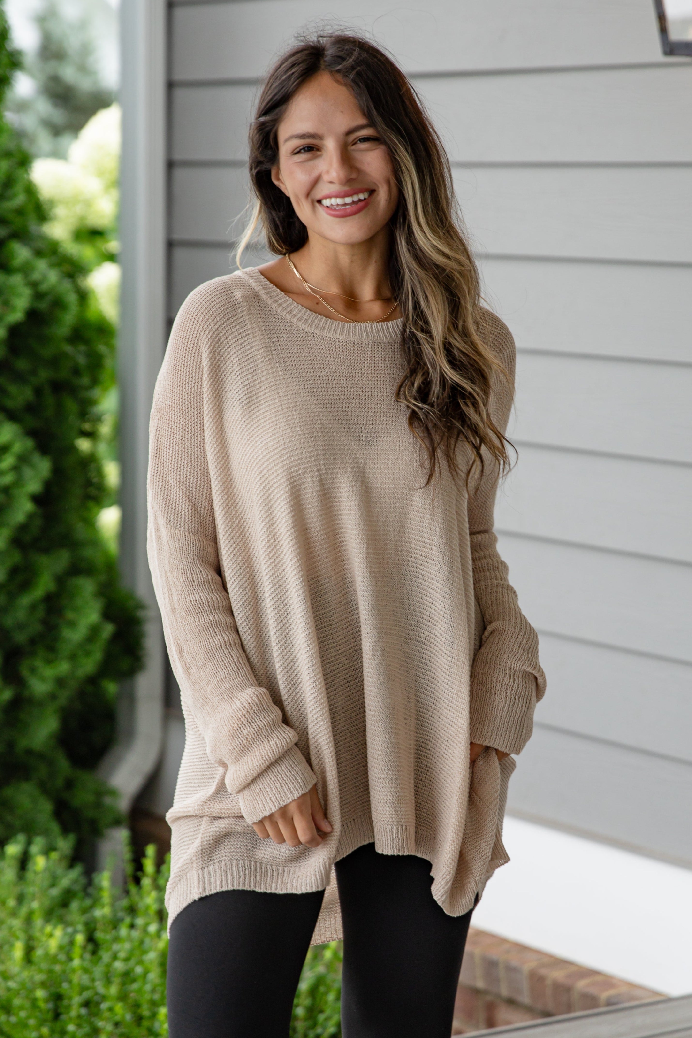 Woman wearing a beige sweater and black leggings standing outdoors.