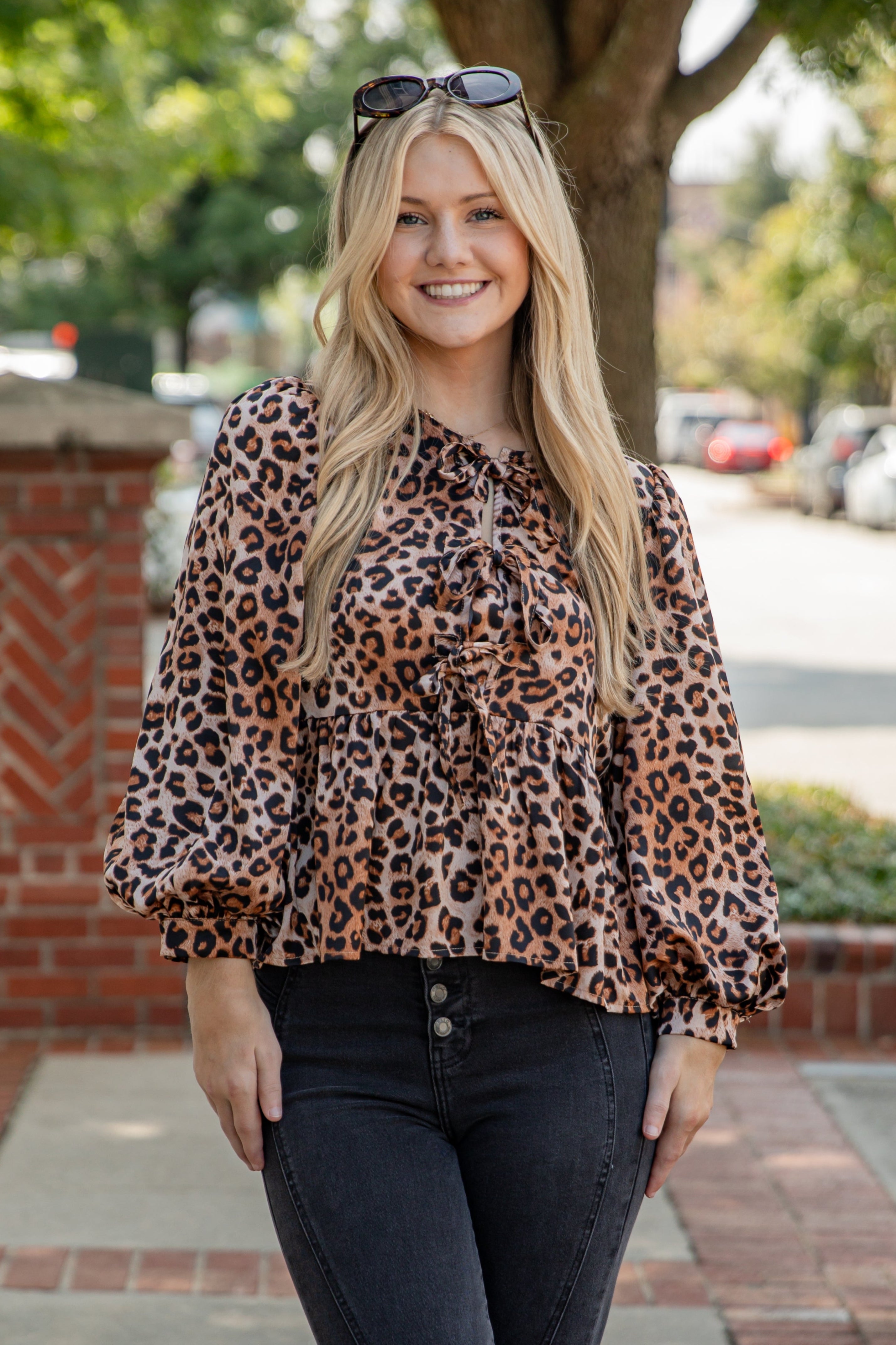 Woman wearing a leopard print blouse and sunglasses outdoors.