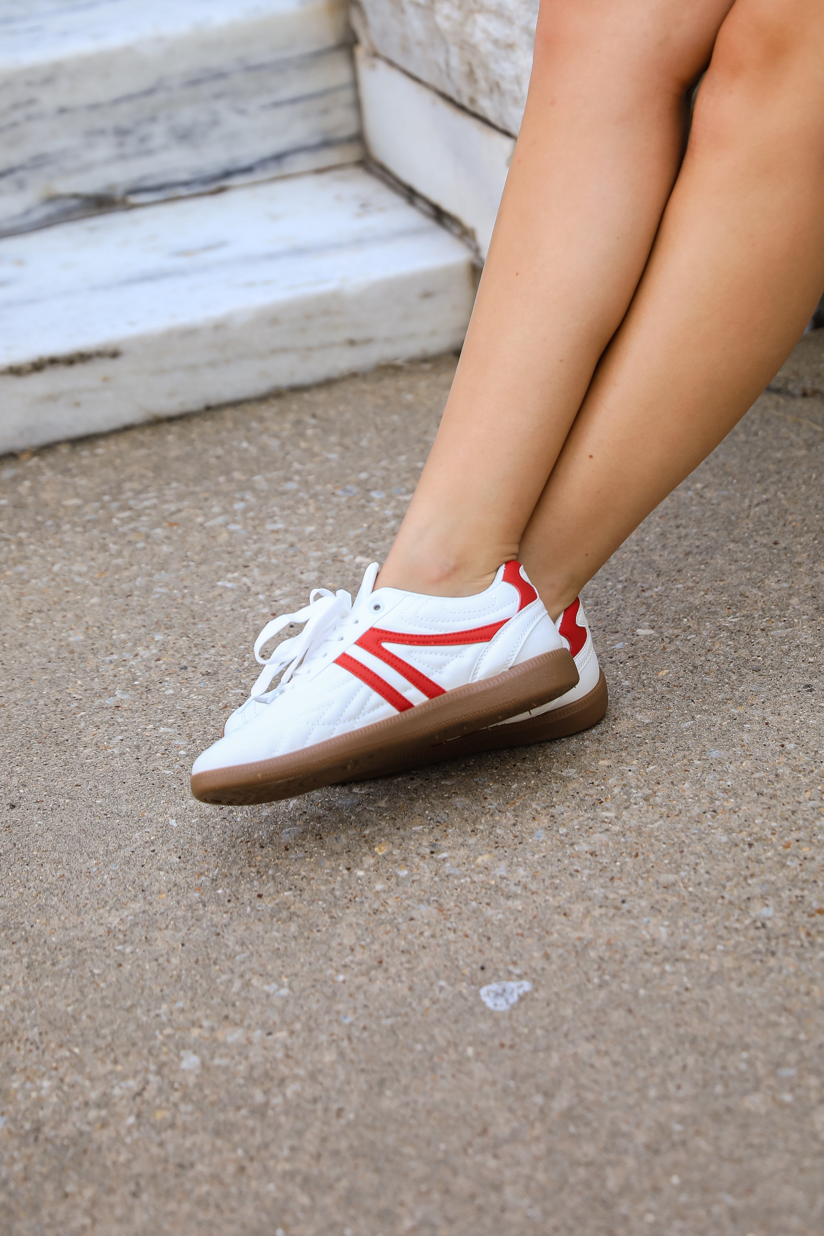White sneakers with red stripes worn by a person on a concrete surface.