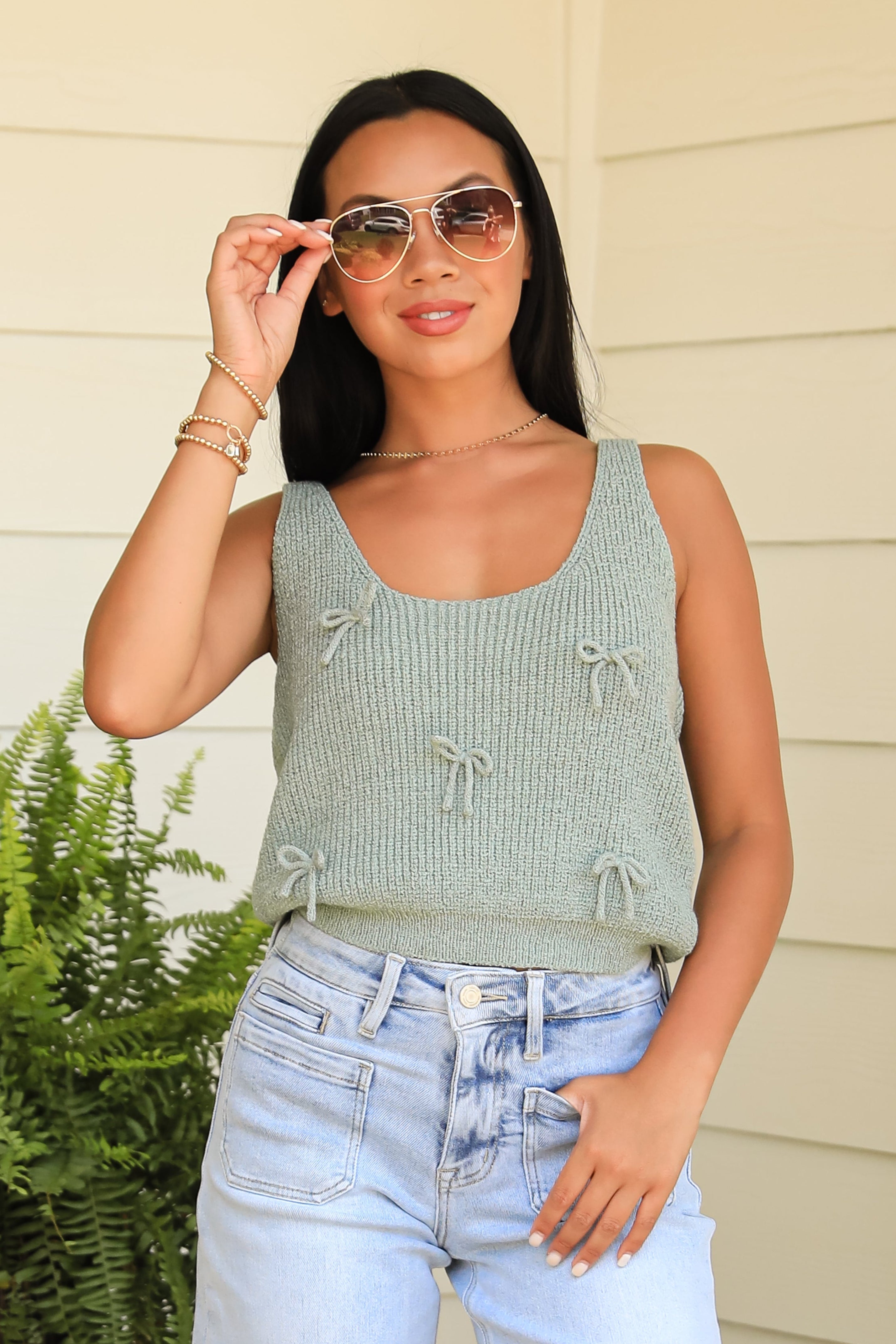 Woman wearing a light green sleeveless top and blue jeans, standing outdoors.