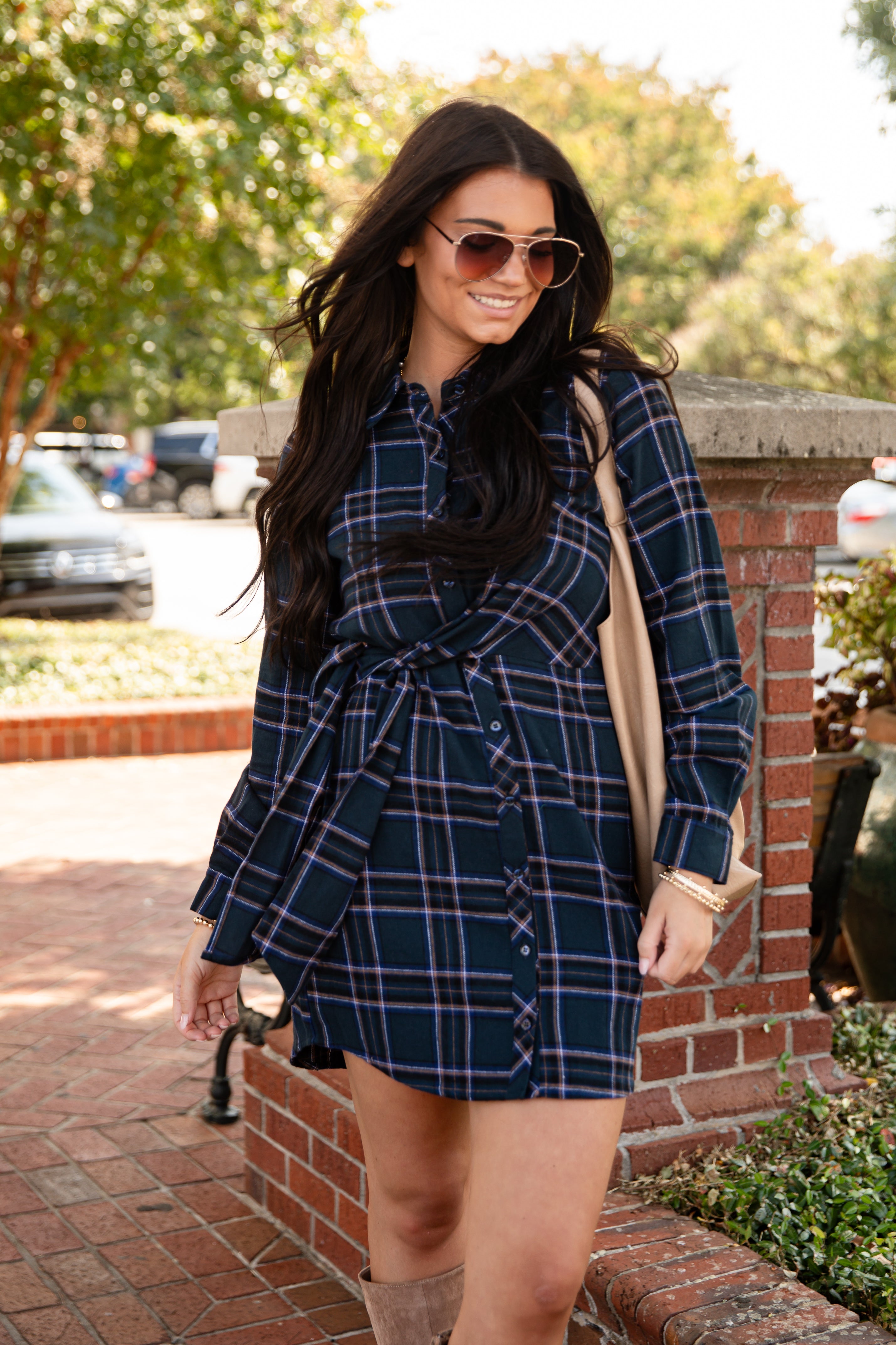Woman wearing a blue plaid dress standing outdoors on a brick path.