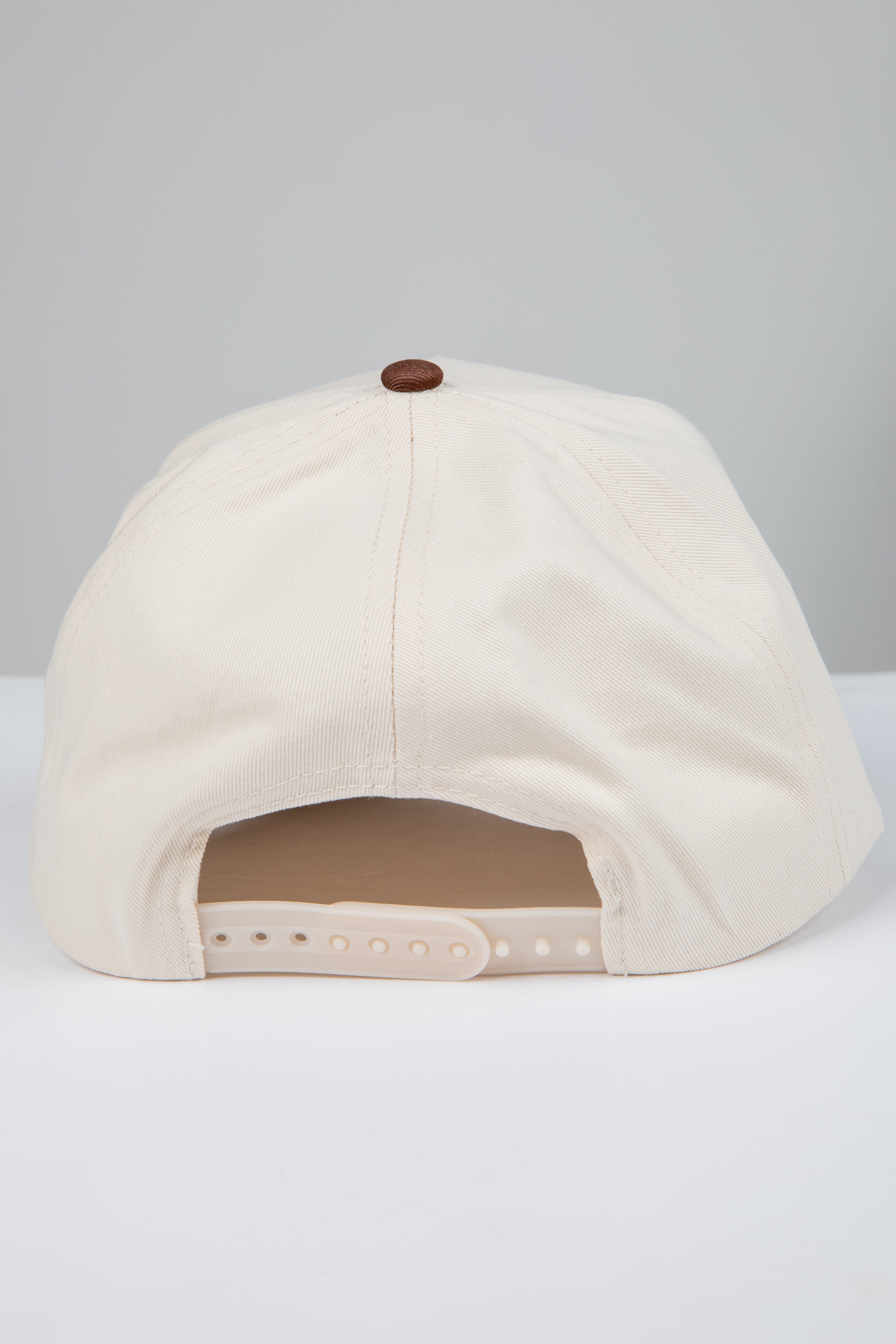 Beige baseball cap with a brown button on a light gray background