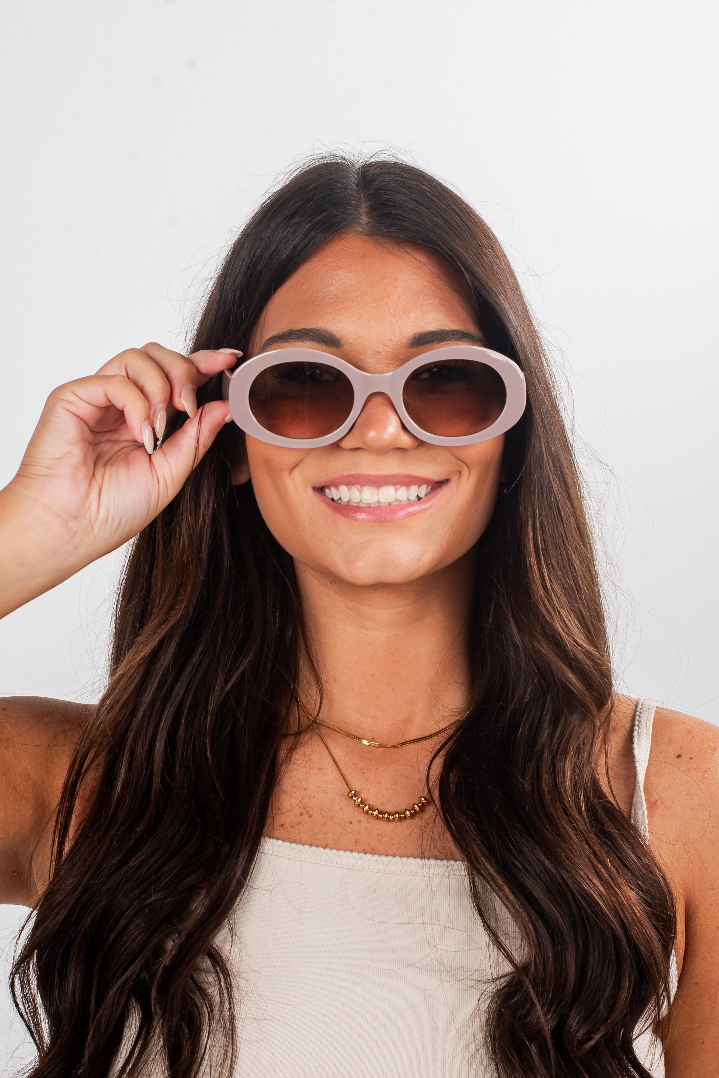 Woman holding a pair of sunglasses in front of her face against a white background